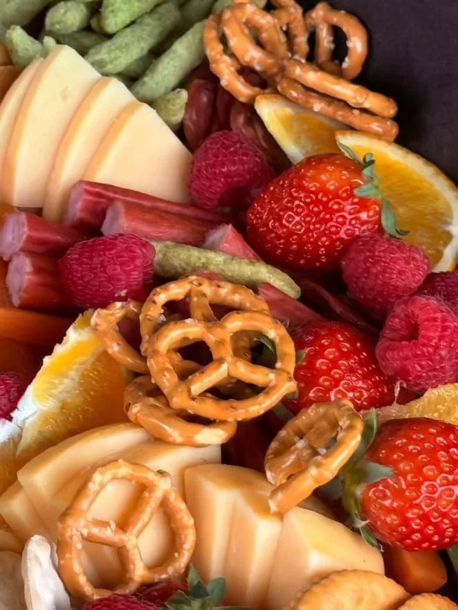Assorted fresh fruits including strawberries, raspberries, orange slices, cheese, pretzels, and green beans.