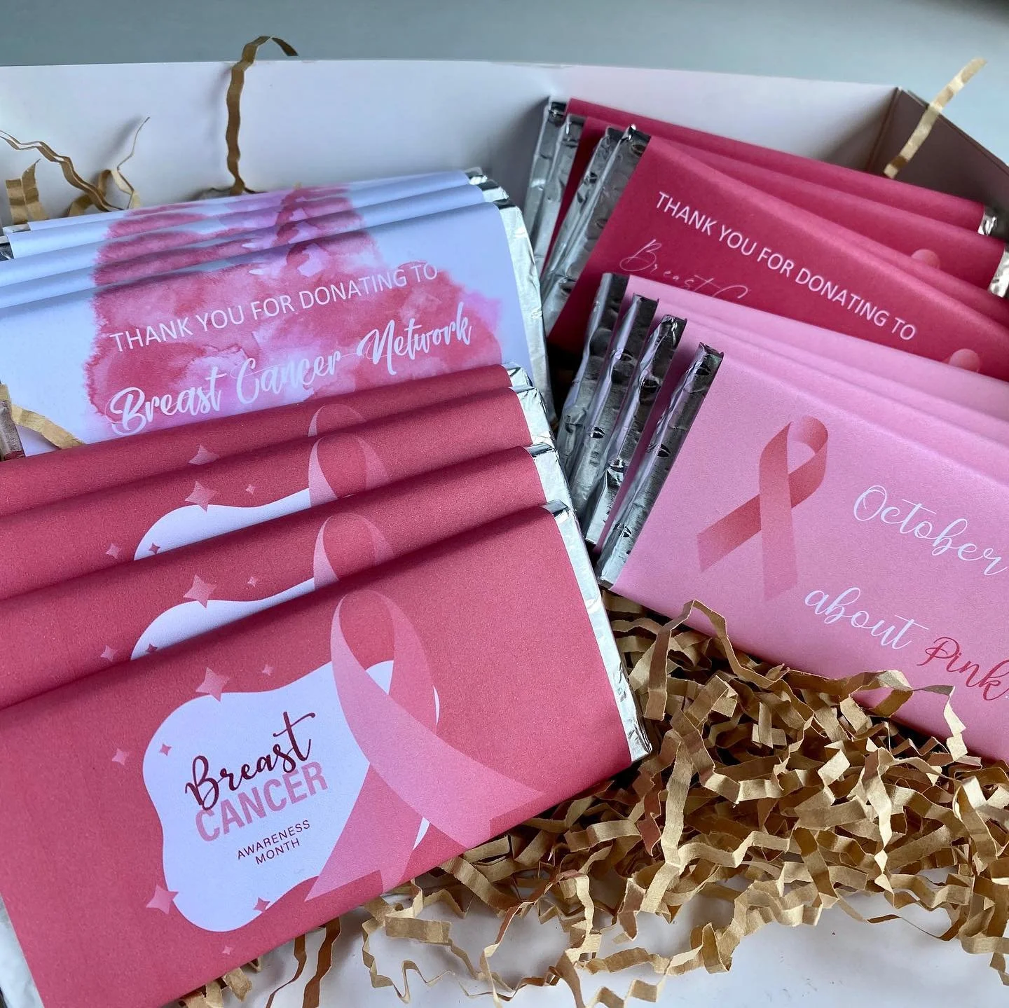 Pink and white brochures and cards with breast cancer awareness messages and ribbons, arranged on shredded paper filler in a box.