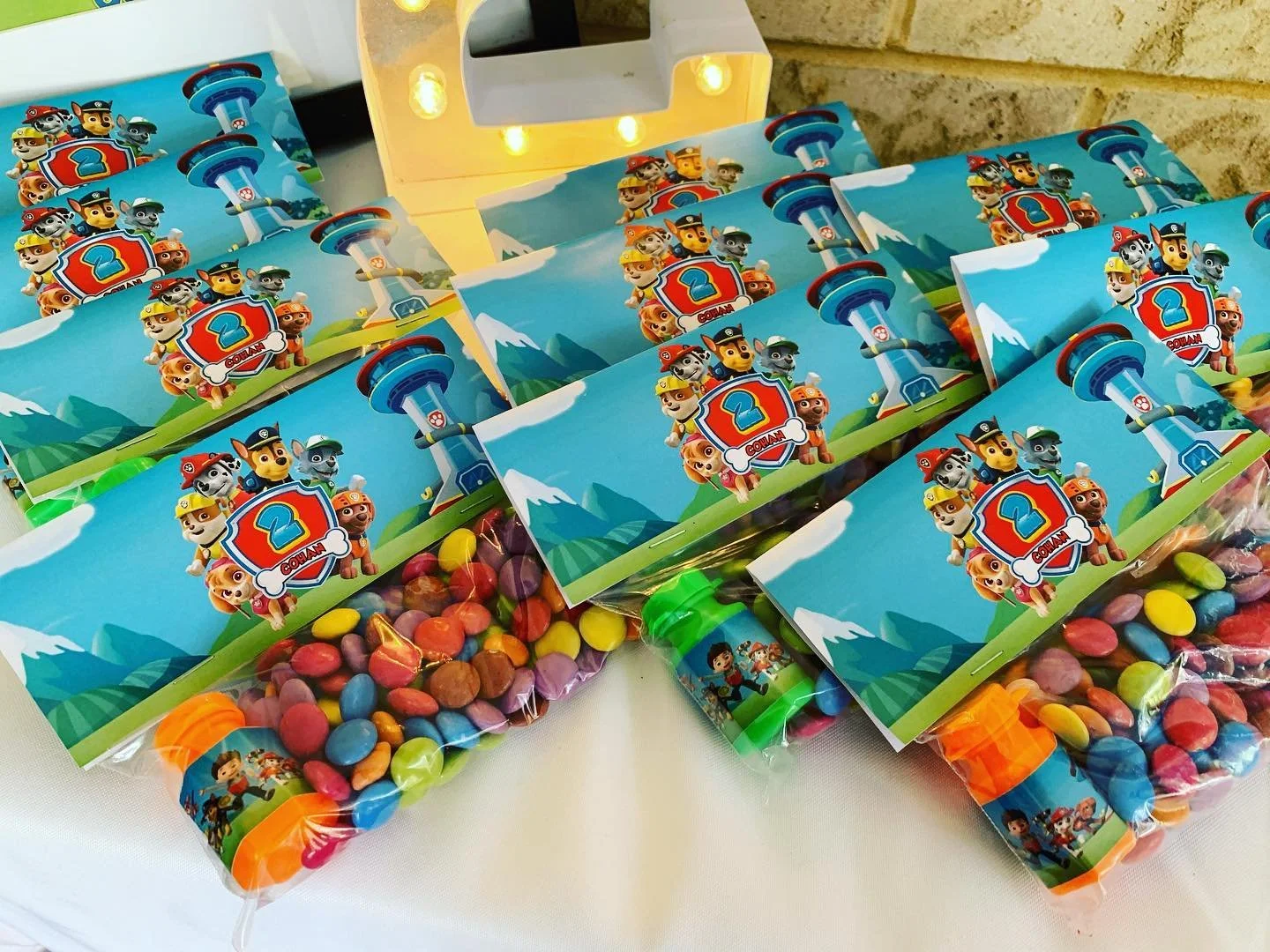 Multiple birthday party favor bags and bottles with Paw Patrol theme featuring characters and mountain scenery.