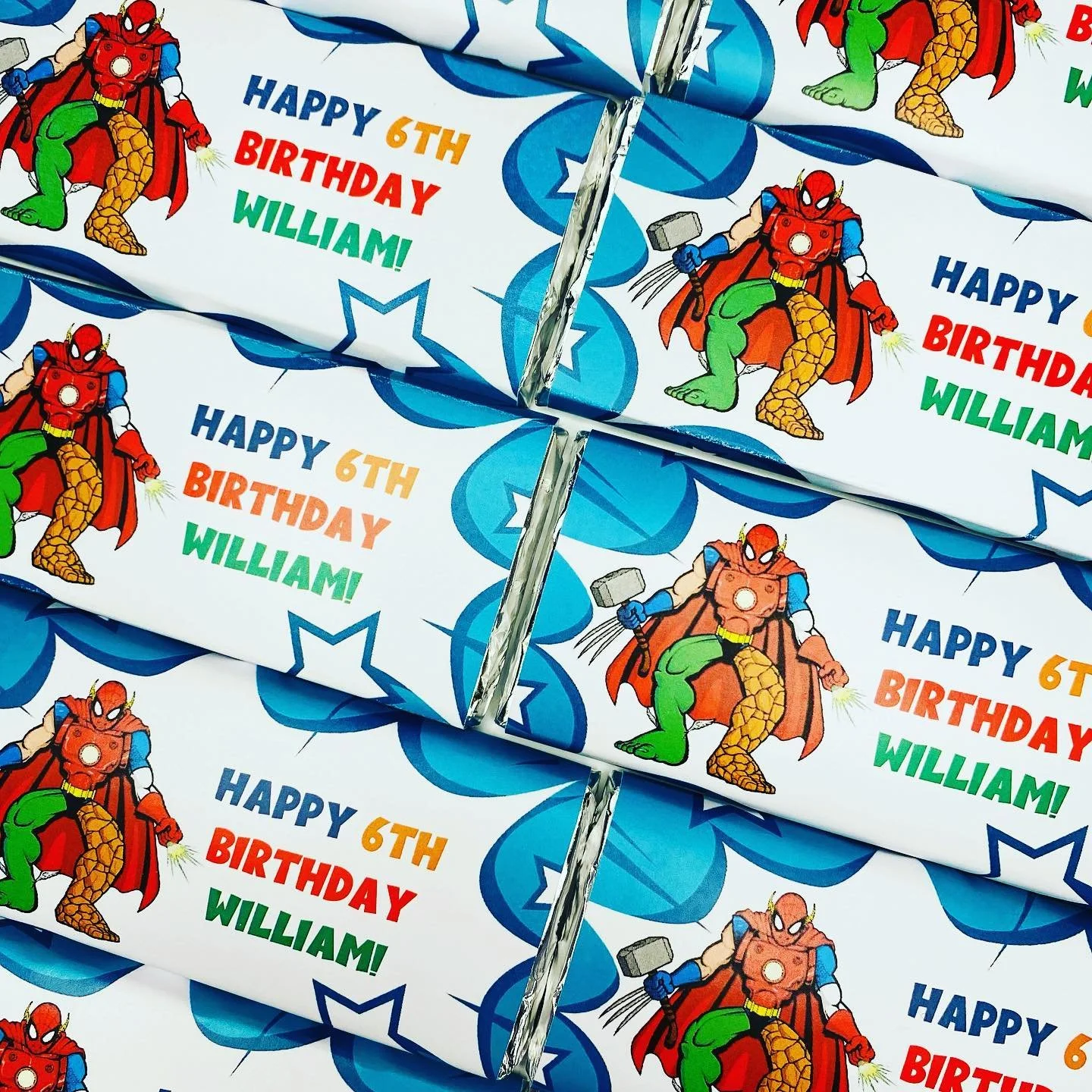 Colorful birthday wrappers featuring Spider-Man dressed as a superhero with a red cape, holding a hammer and a lightning bolt, with birthday message for William's 6th birthday.