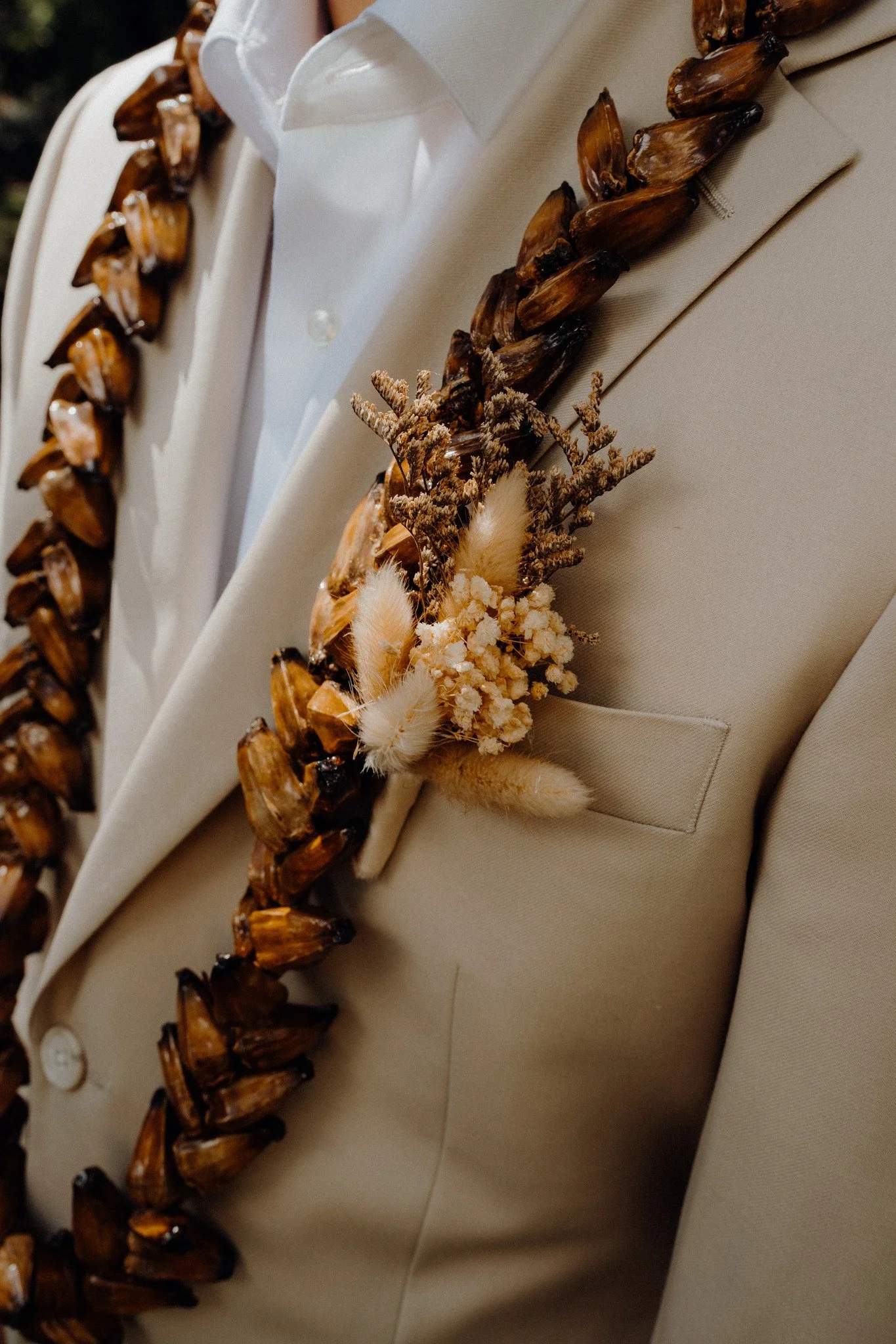 Close-up of a beige tuxedo with a floral boutonnire and wooden beaded necklace.
