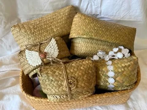 Various woven straw baskets and containers with decorative flowers and a small angel figurine.