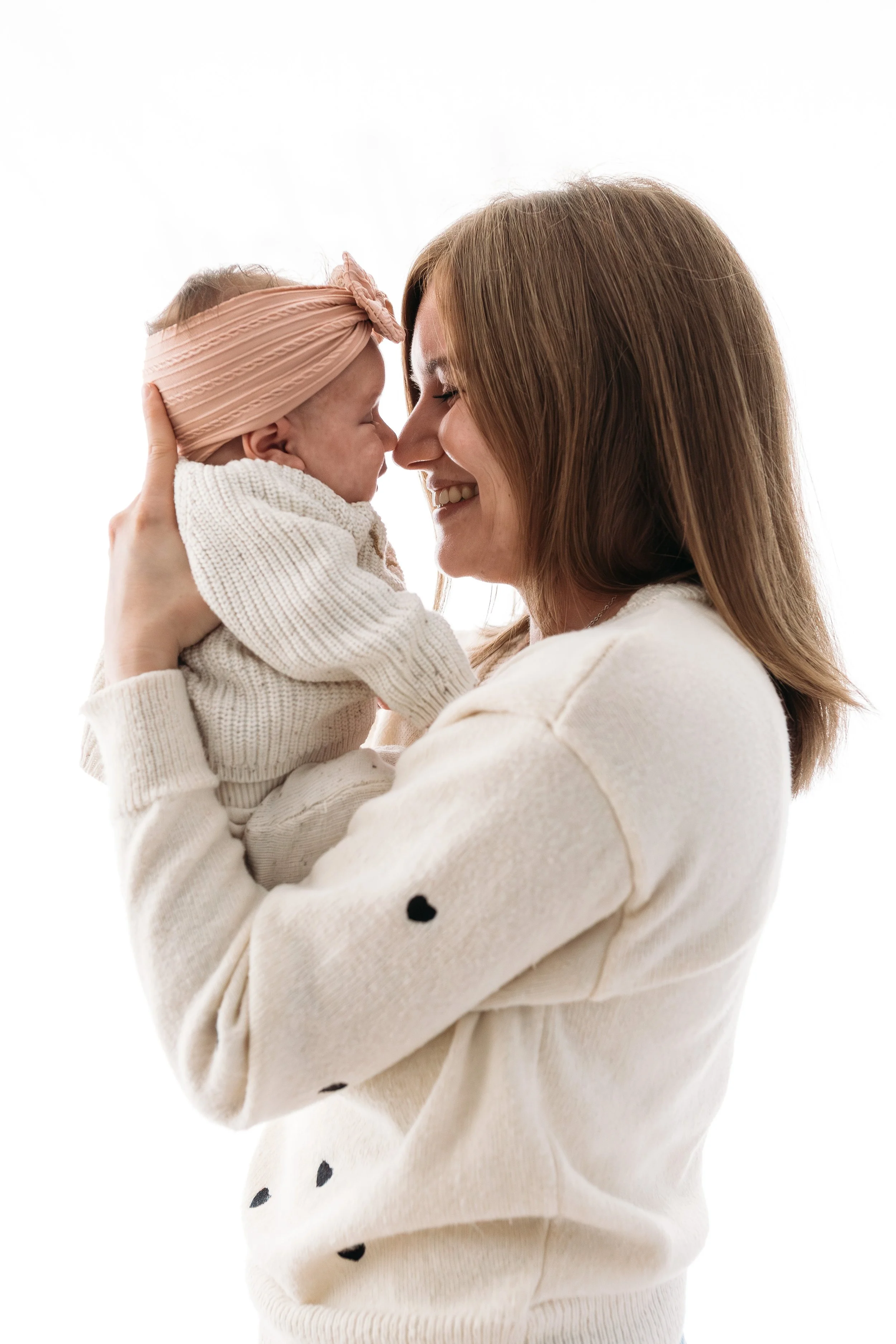 A woman holding a smiling baby girl close to her face, both with their eyes closed, against a white background.