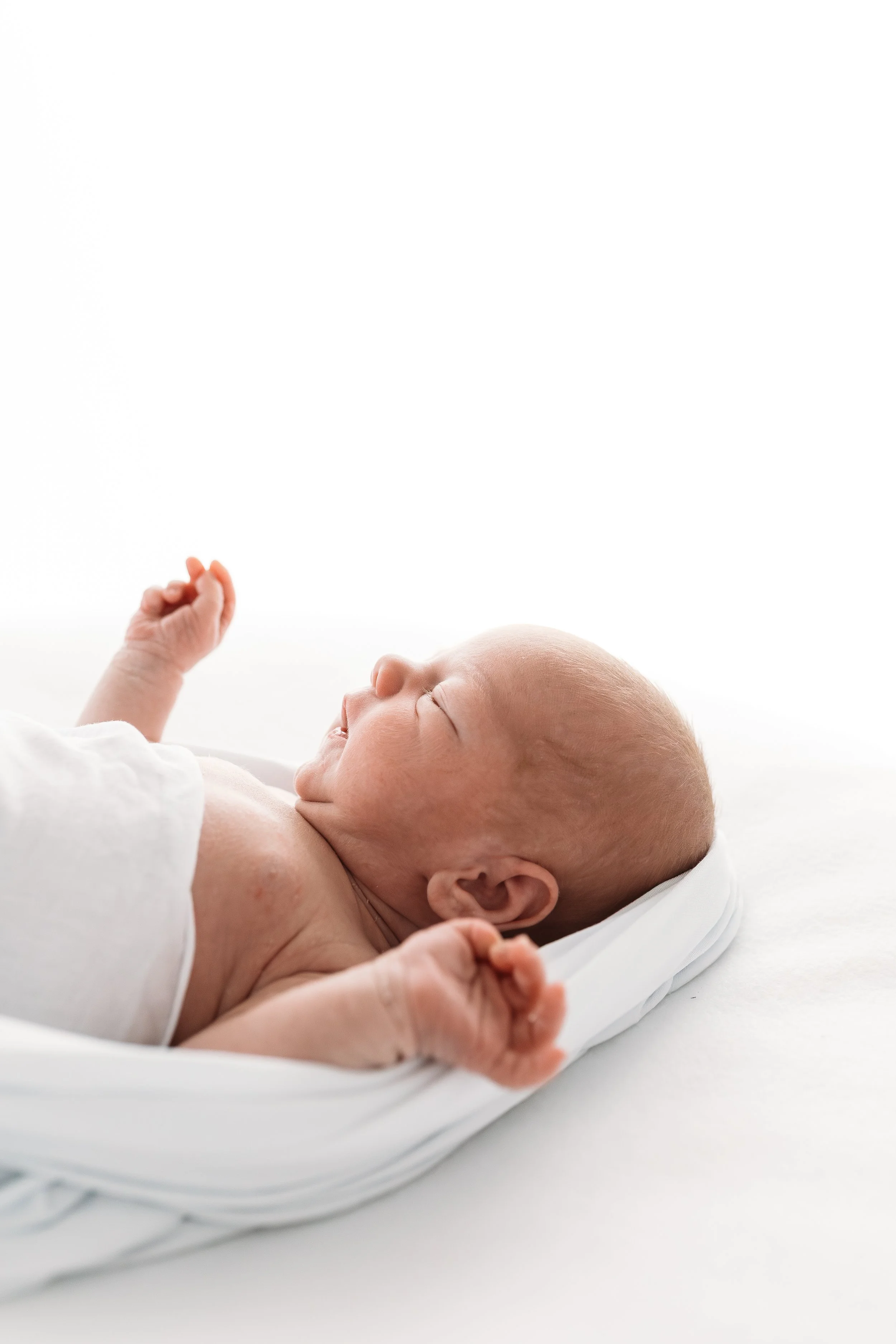 Close-up of a sleeping newborn baby lying on a white bed, with a peaceful expression and tiny hands.