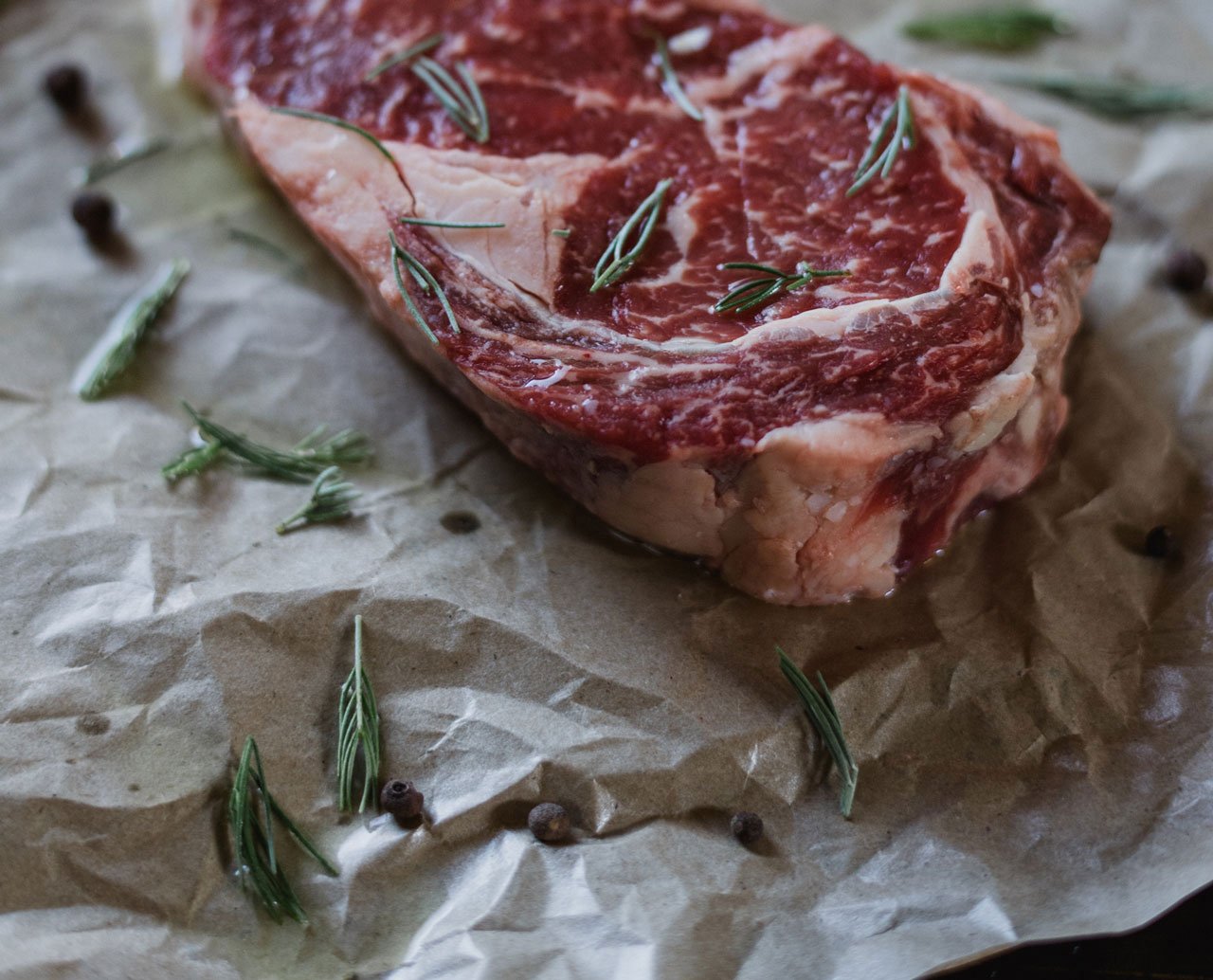 En rå bøf med krydderurter og peberkorn på brunt bagepapir.