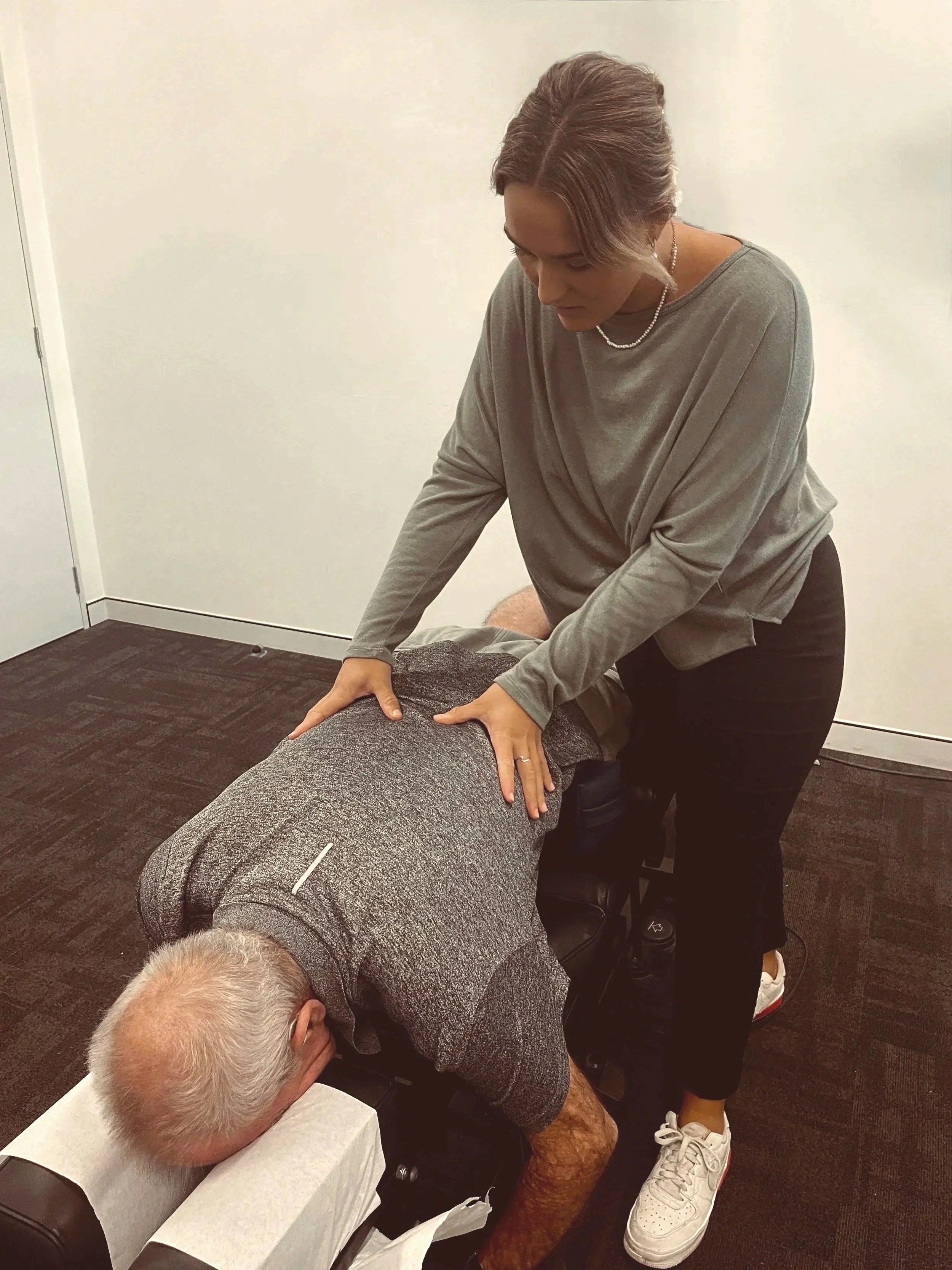 A person giving a massage to another person lying face down on a massage table in a room with plain walls.