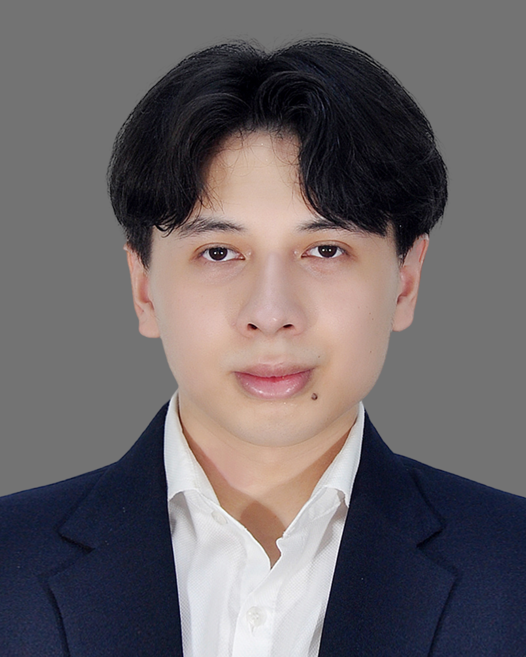 Portrait of a young man with dark hair, wearing a navy blazer and white shirt, against a gray background.