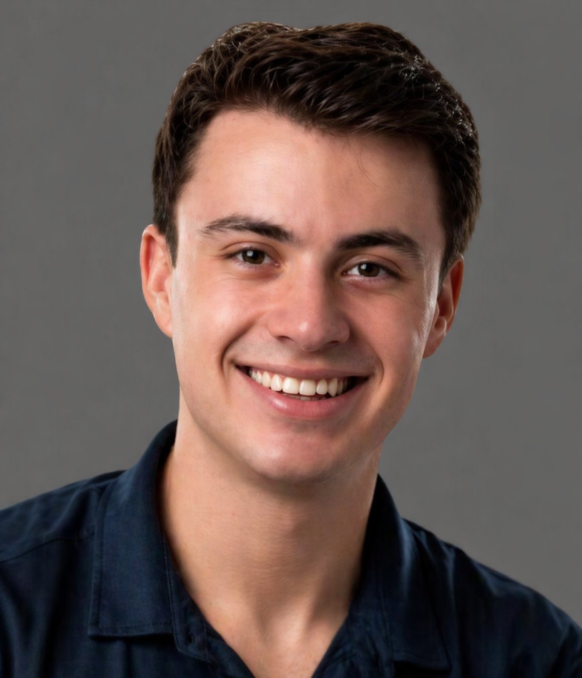 Portrait of a young man with short dark hair, smiling, wearing a dark button-up shirt against a gray background.