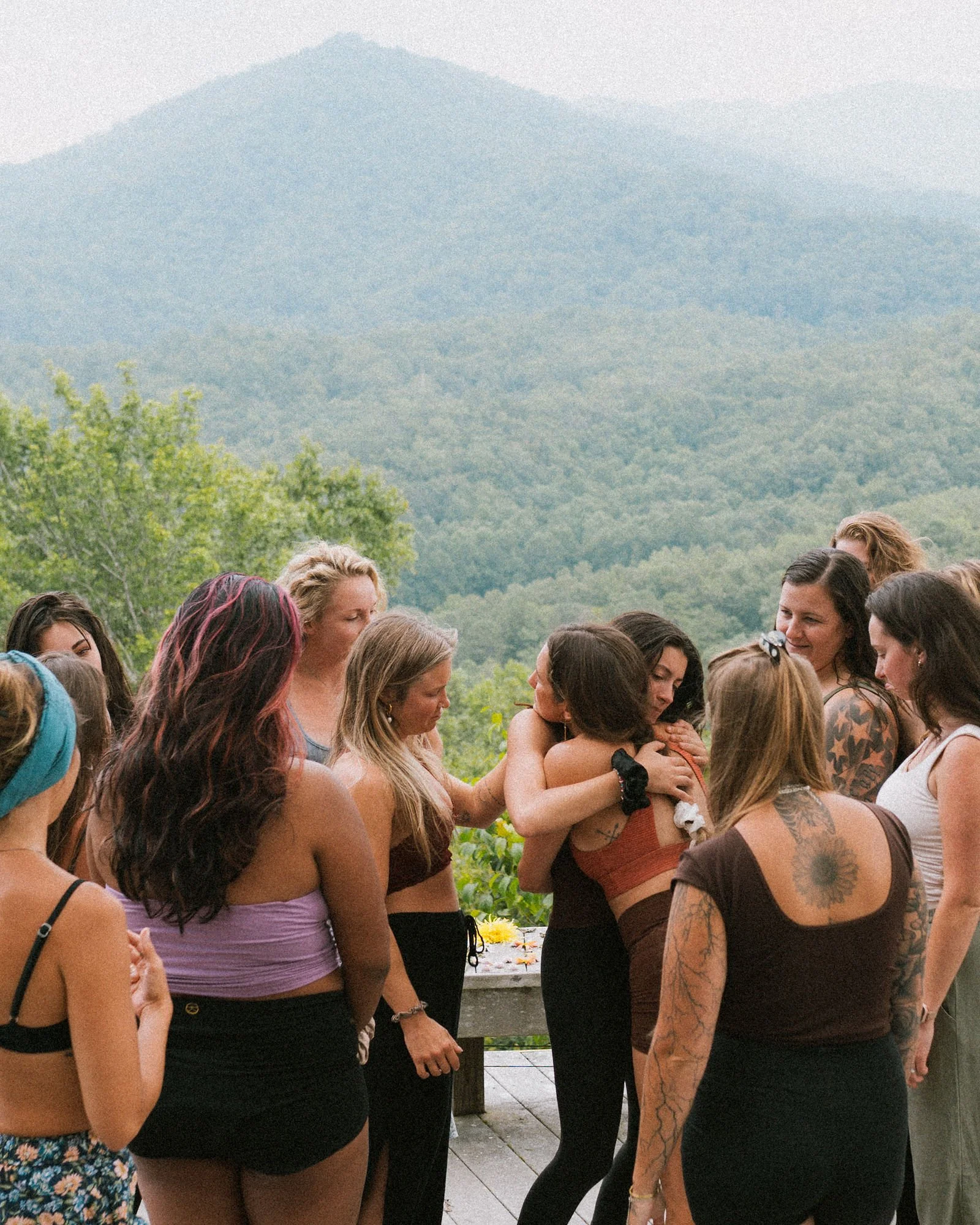 A group of people standing outdoors, with mountains and greenery in the background, participating in a memorial or gathering.