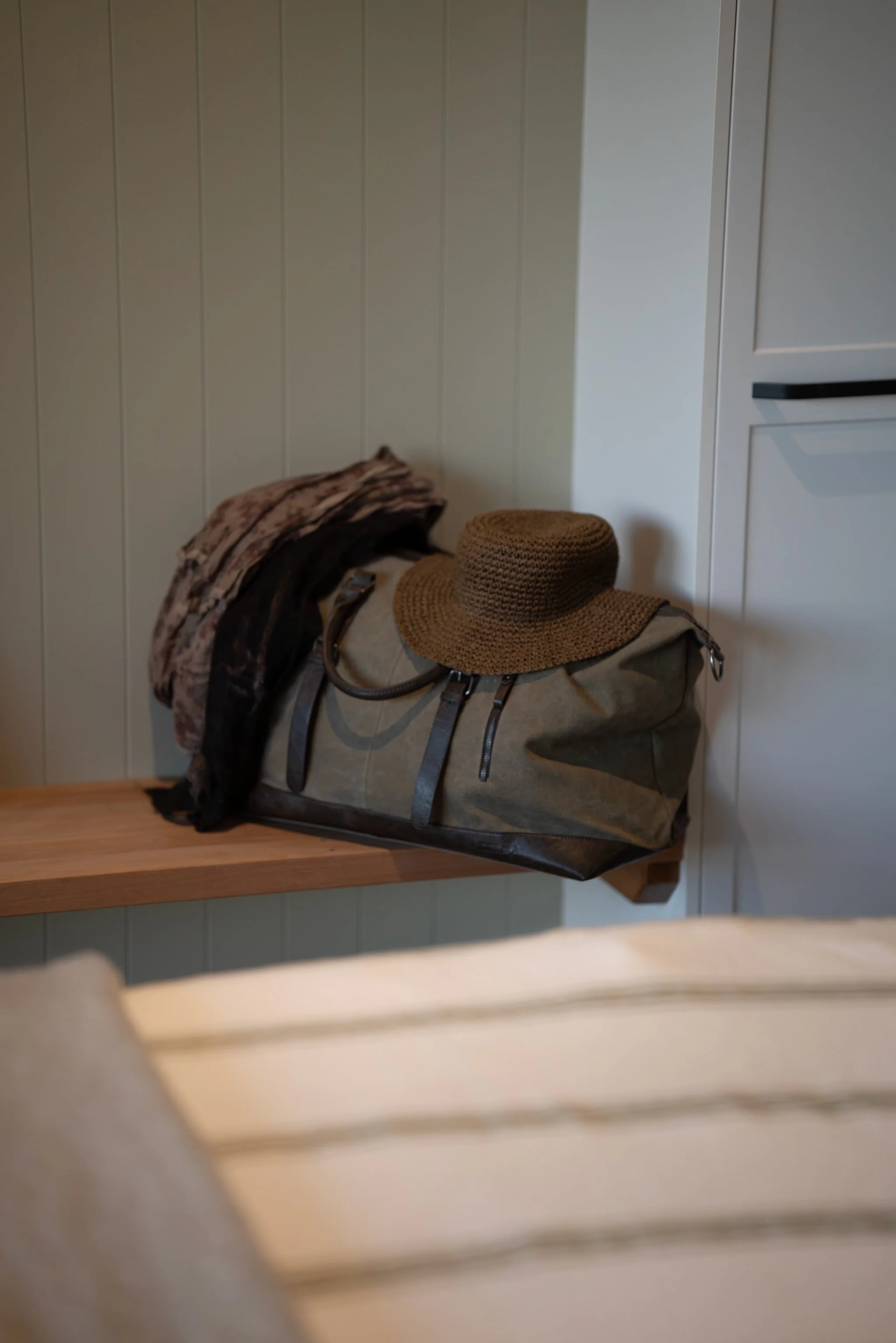 Travel bag and woven hat on wooden shelf in Maunga Tipu studio entryway, evoking slow travel and unhurried arrival at luxury Fiordland retreat