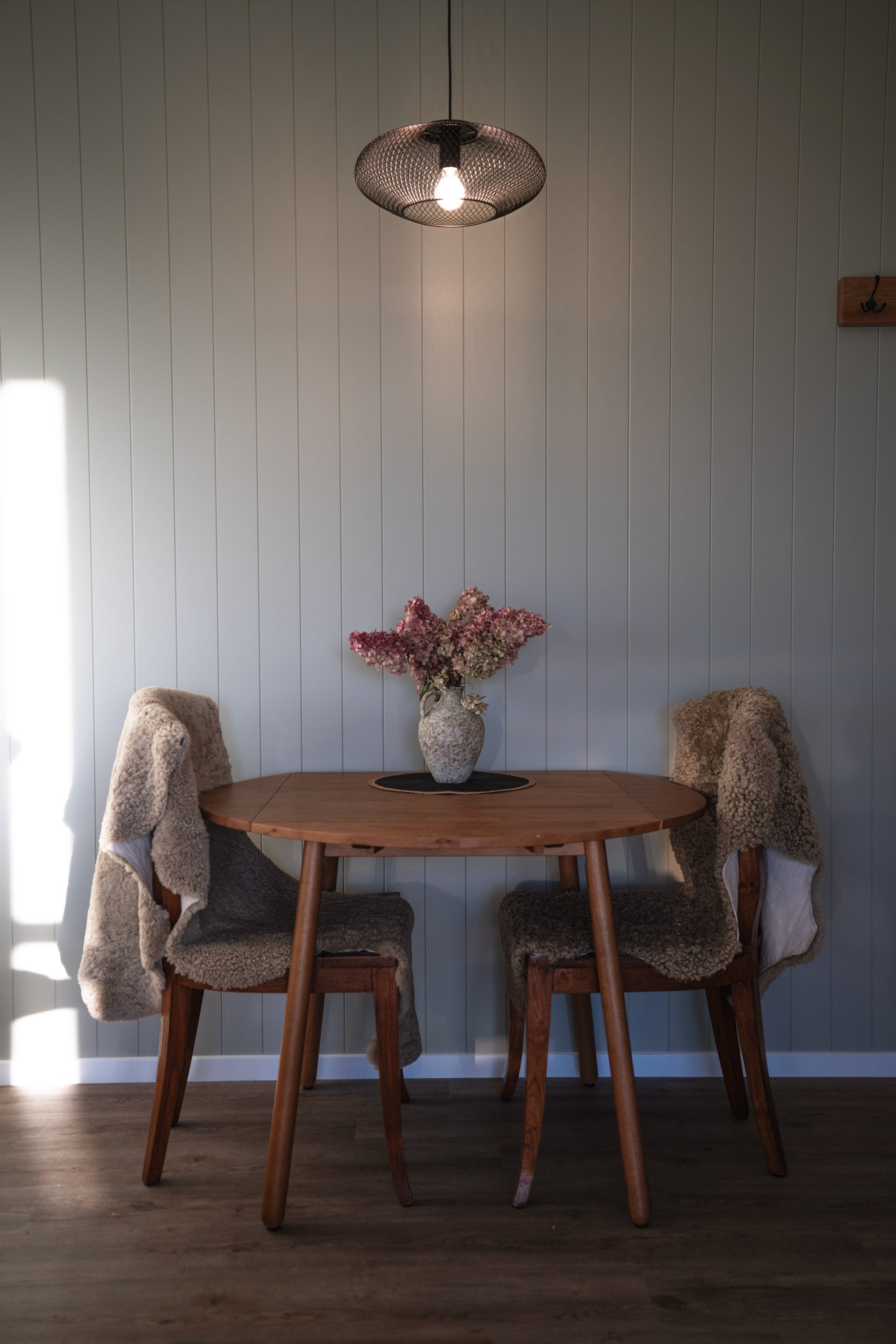 Minimalist wooden table and chairs in Maunga Tipu studio with white shiplap walls and natural light, designed for intimate dining