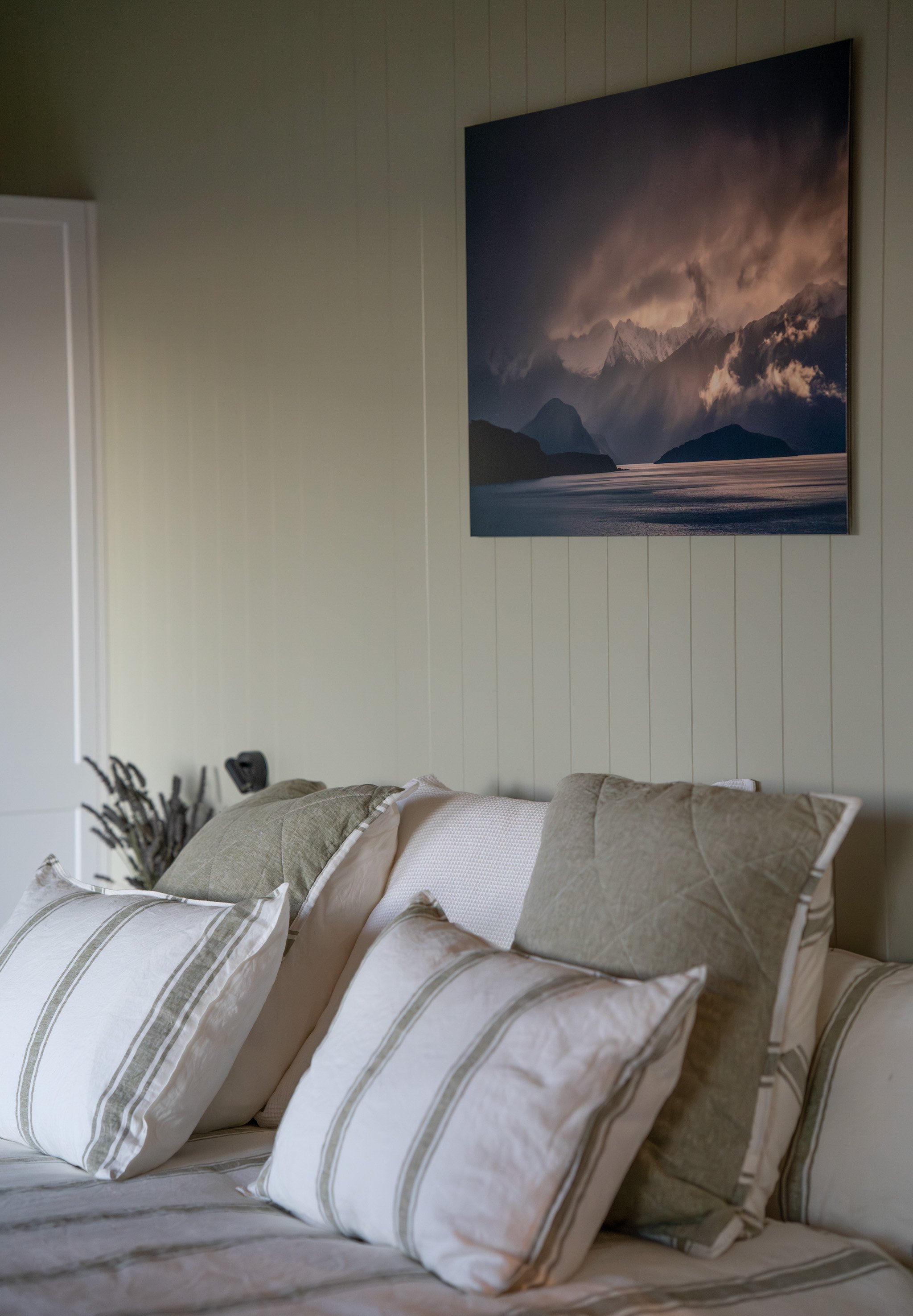 Natural linen bedding and layered pillows in Maunga Tipu studio with Fiordland mountain artwork on white shiplap walls