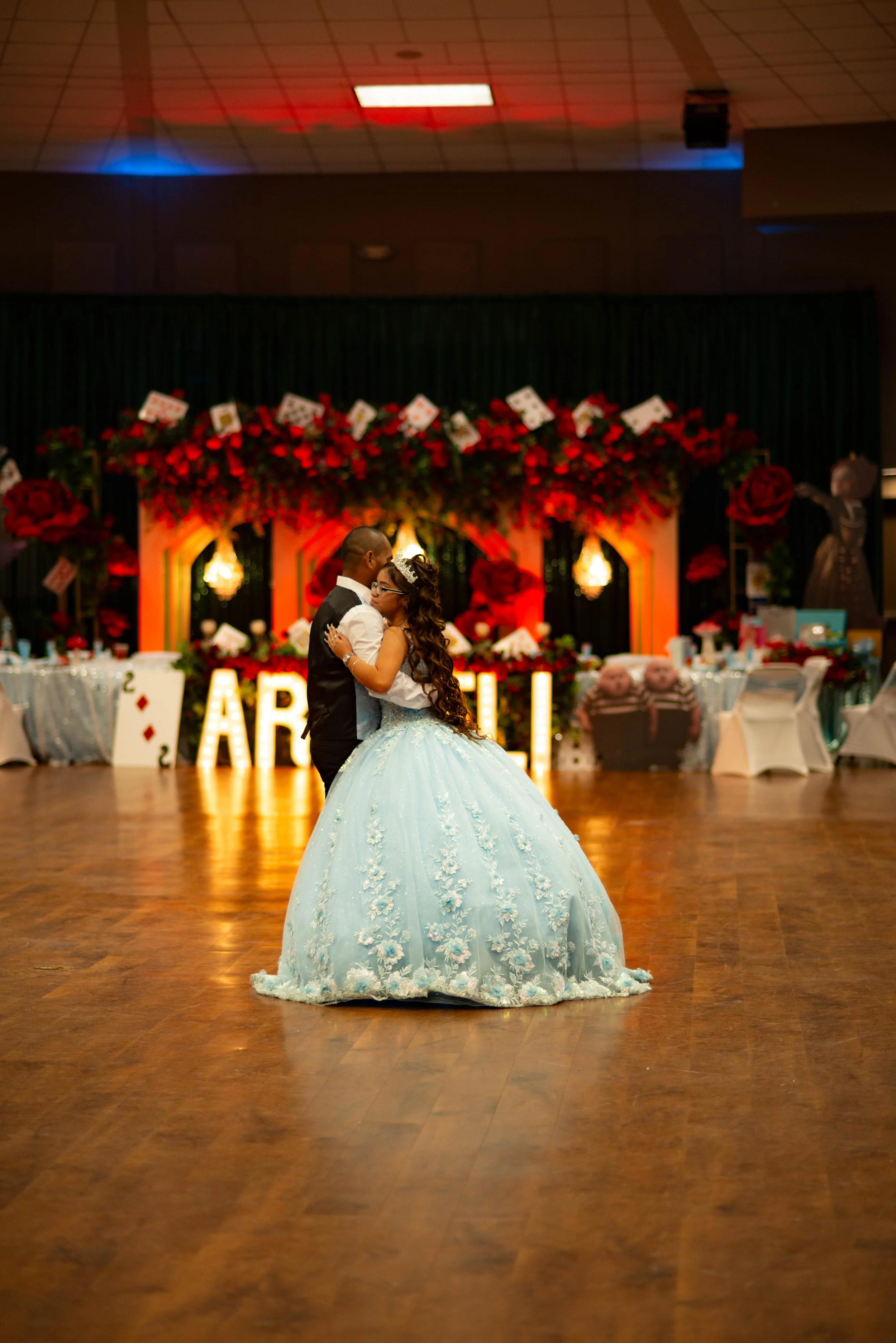 Couple dancing at a formal event with decorated backdrop and large illuminated letters spelling "AR” in the background.
