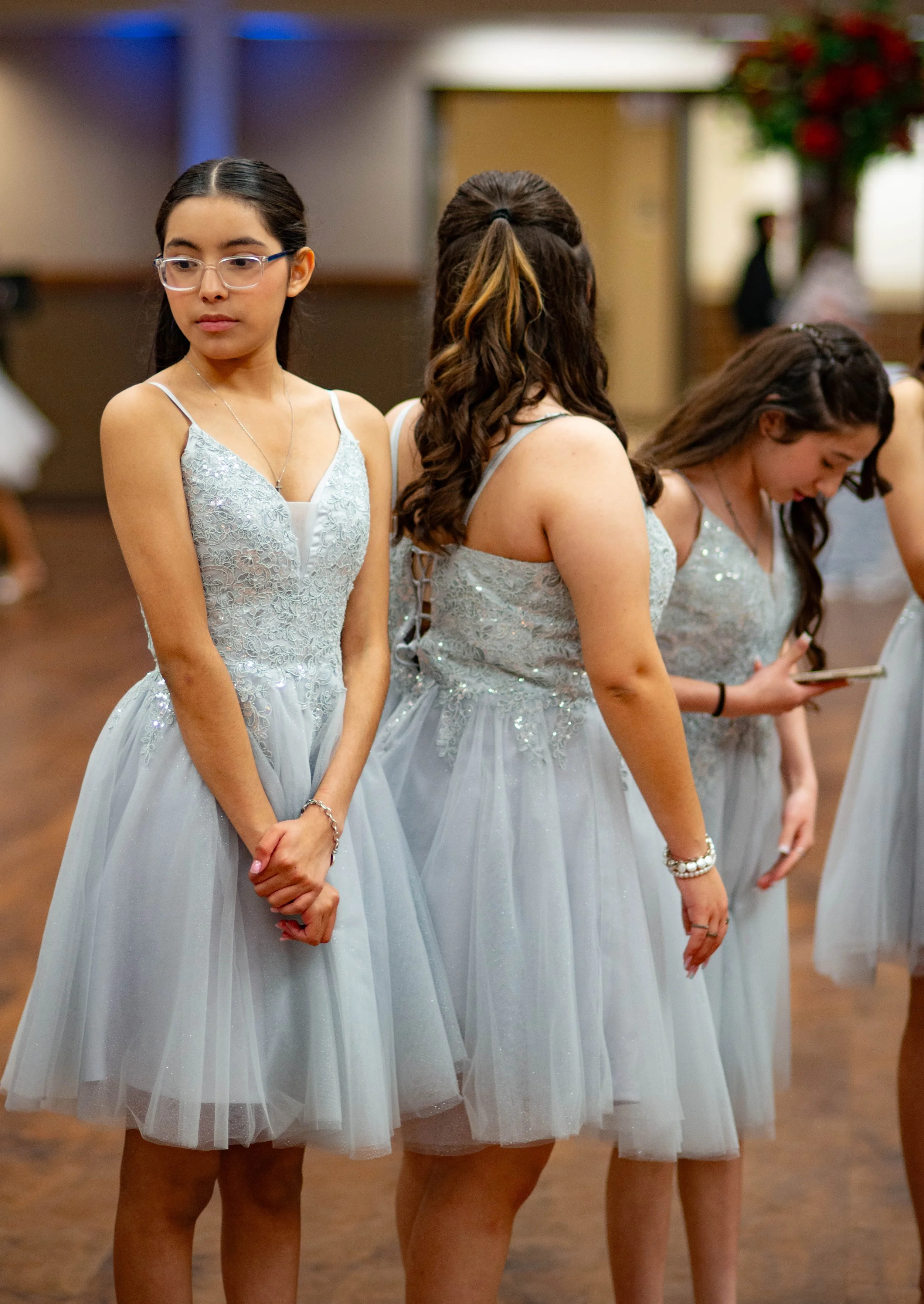Group of young women in matching light blue, lace and tulle dresses at a formal event, standing in a line indoors.