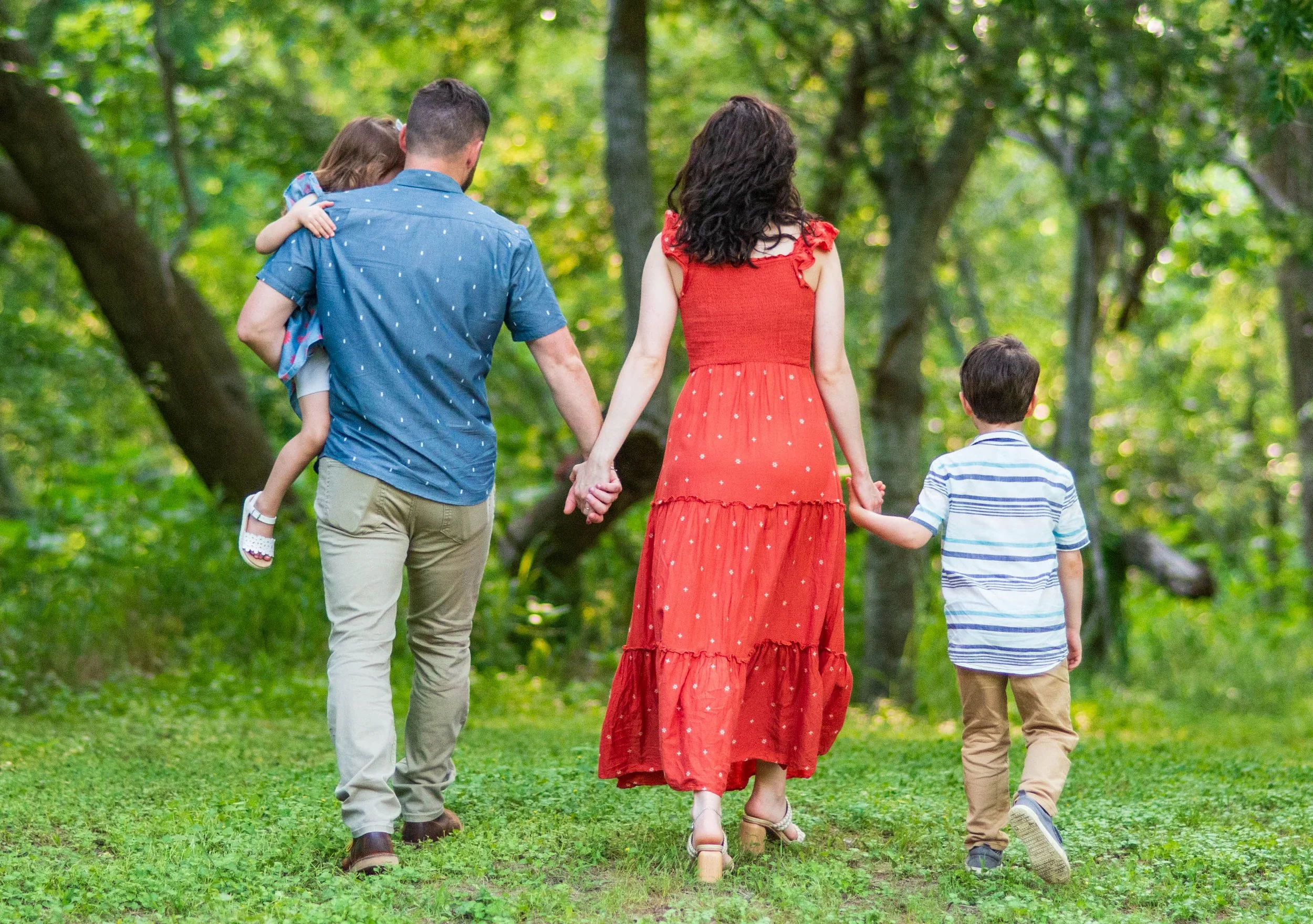 A family of four walking hand-in-hand through a lush green forest during daytime, with trees and foliage surrounding them.