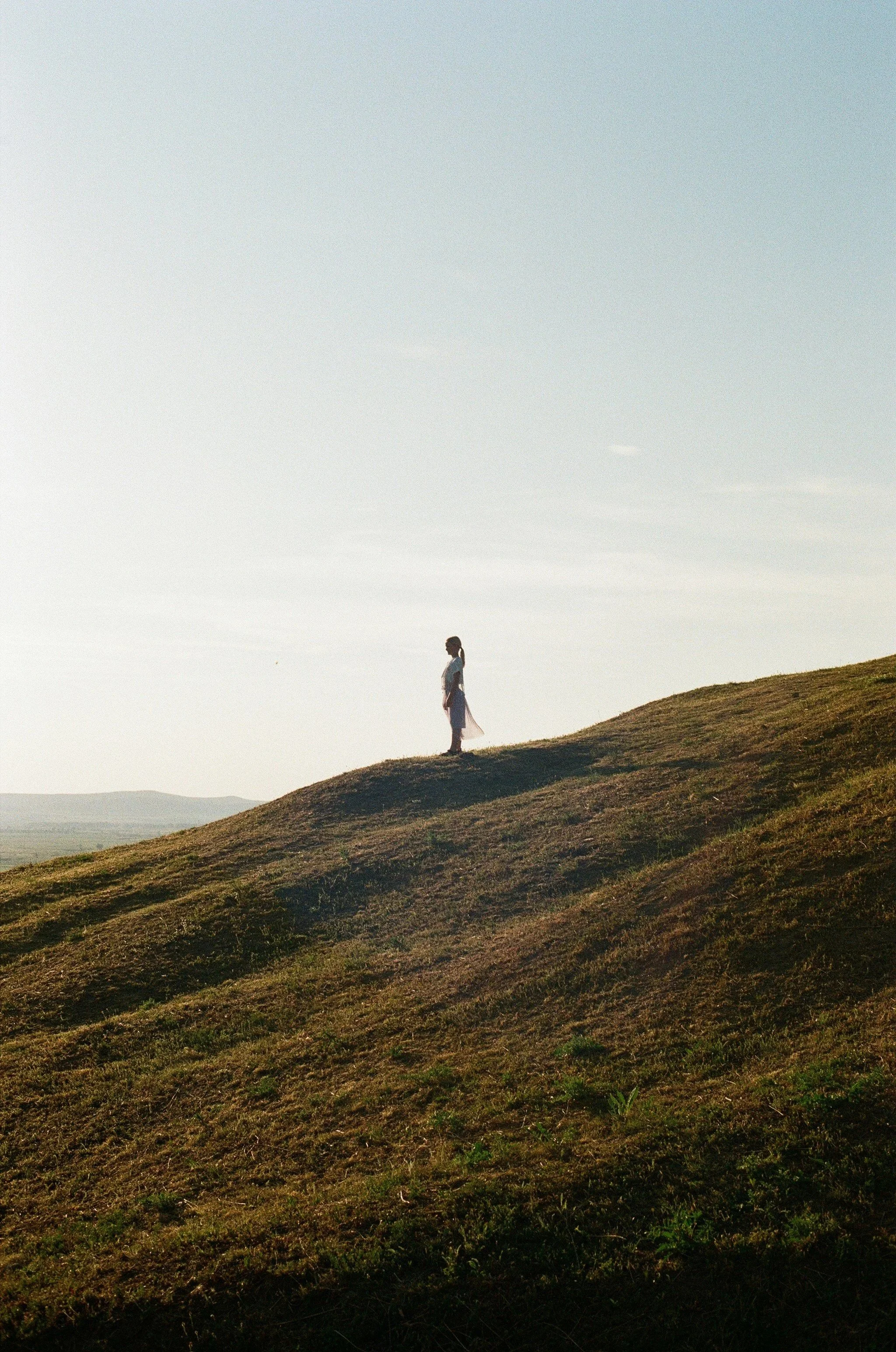 A person standing on a grassy hill with a clear sky in the background.