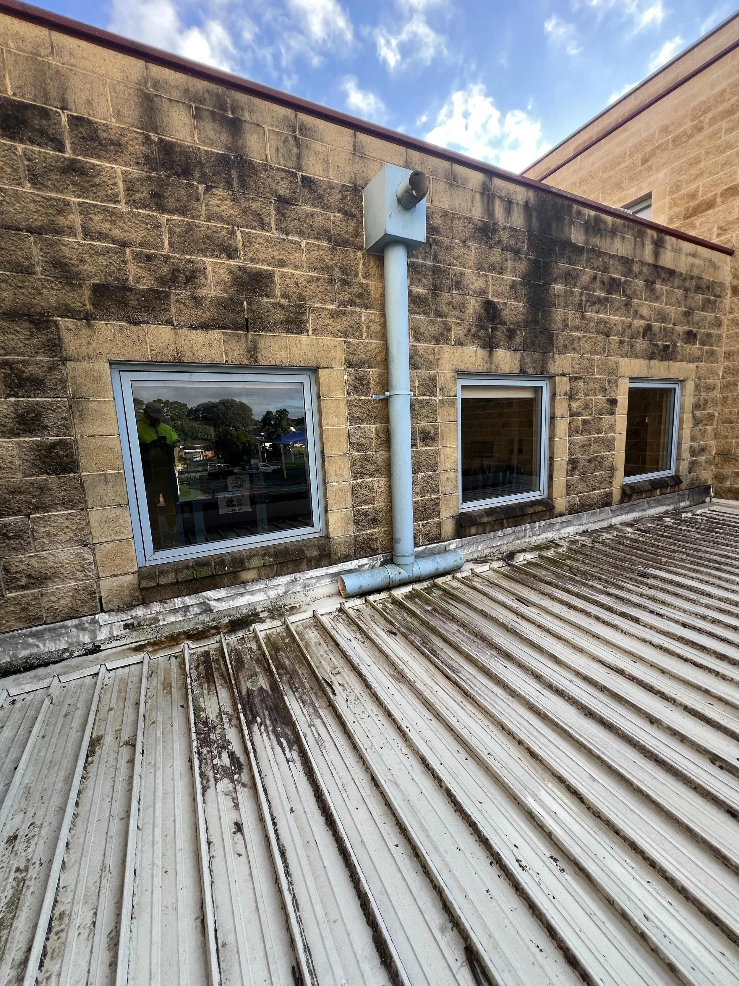 Exterior view of a building with two windows and a drainage pipe, with a brick wall and a cloudy sky.