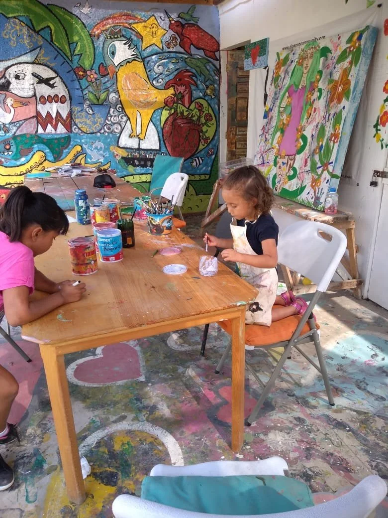 Niñas pintando en un taller de arte, rodeadas de pinturas y murales coloridos en las paredes.