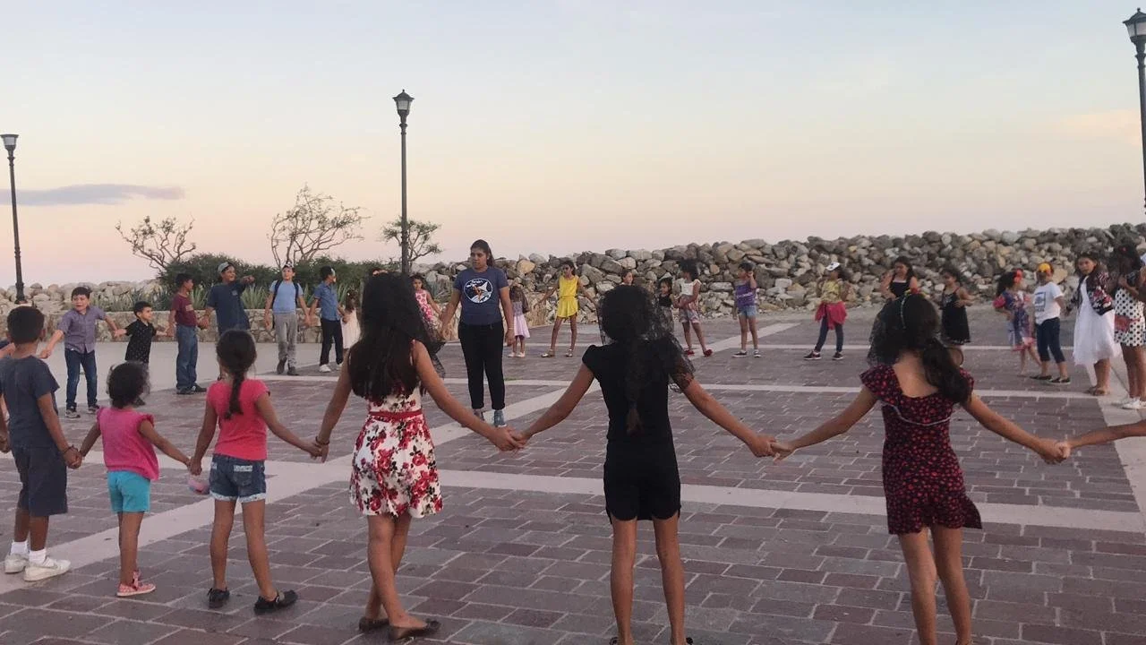 Niños y niñas formando un círculo en un espacio público al atardecer.