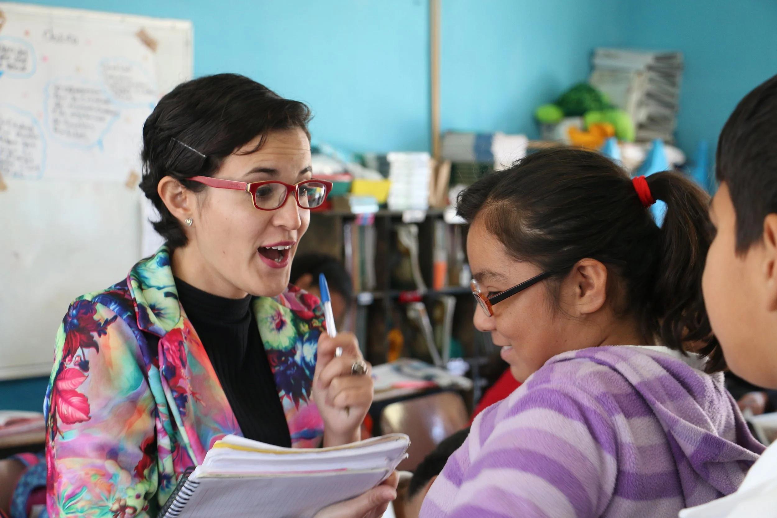 Una maestra habla con dos alumnos en un aula escolar.