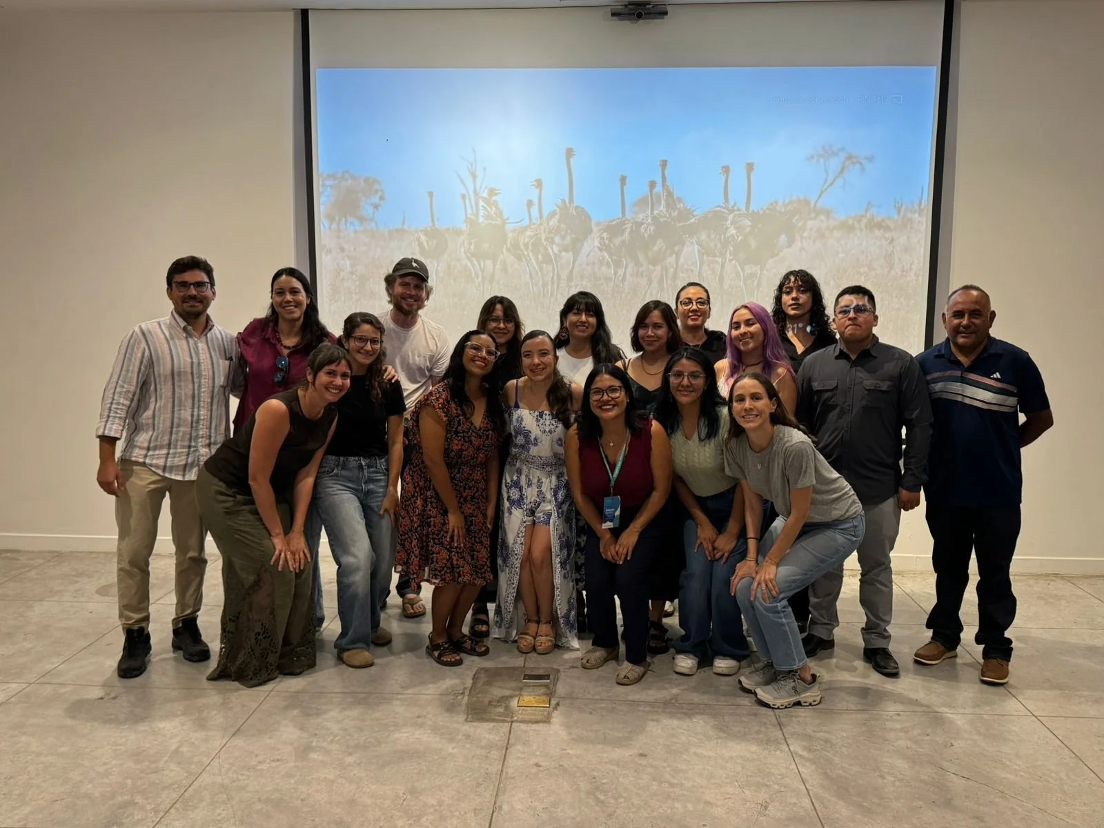 Grupo de personas posando en un evento con una presentación de fondo.