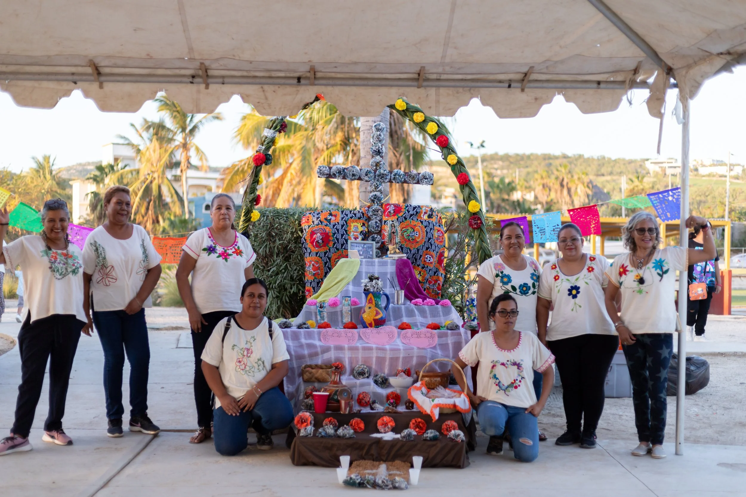 Grupo de mujeres en una celebración tradicional mexicana con ofrenda y decoraciones coloridas.