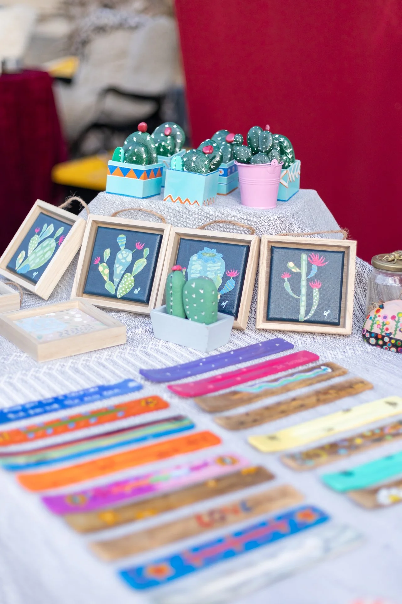 Arte y manualidades en una mesa, con figuras de cactus y cuadros decorativos con cactus pintados.