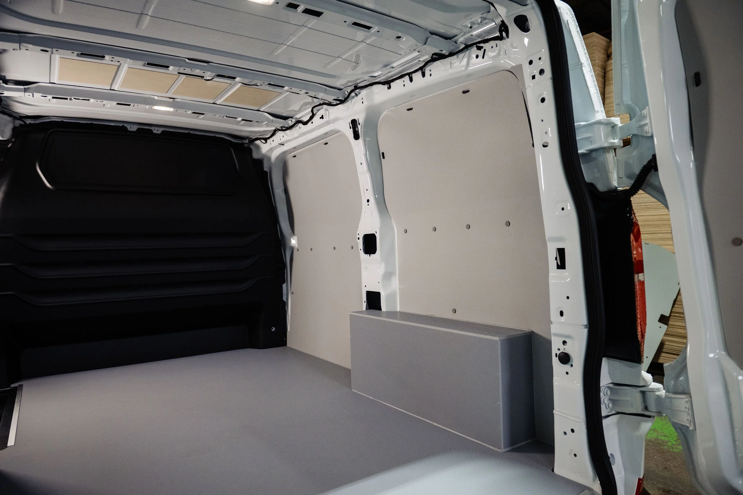 Interior of a cargo van with empty, insulated walls, and a gray storage box on the floor.