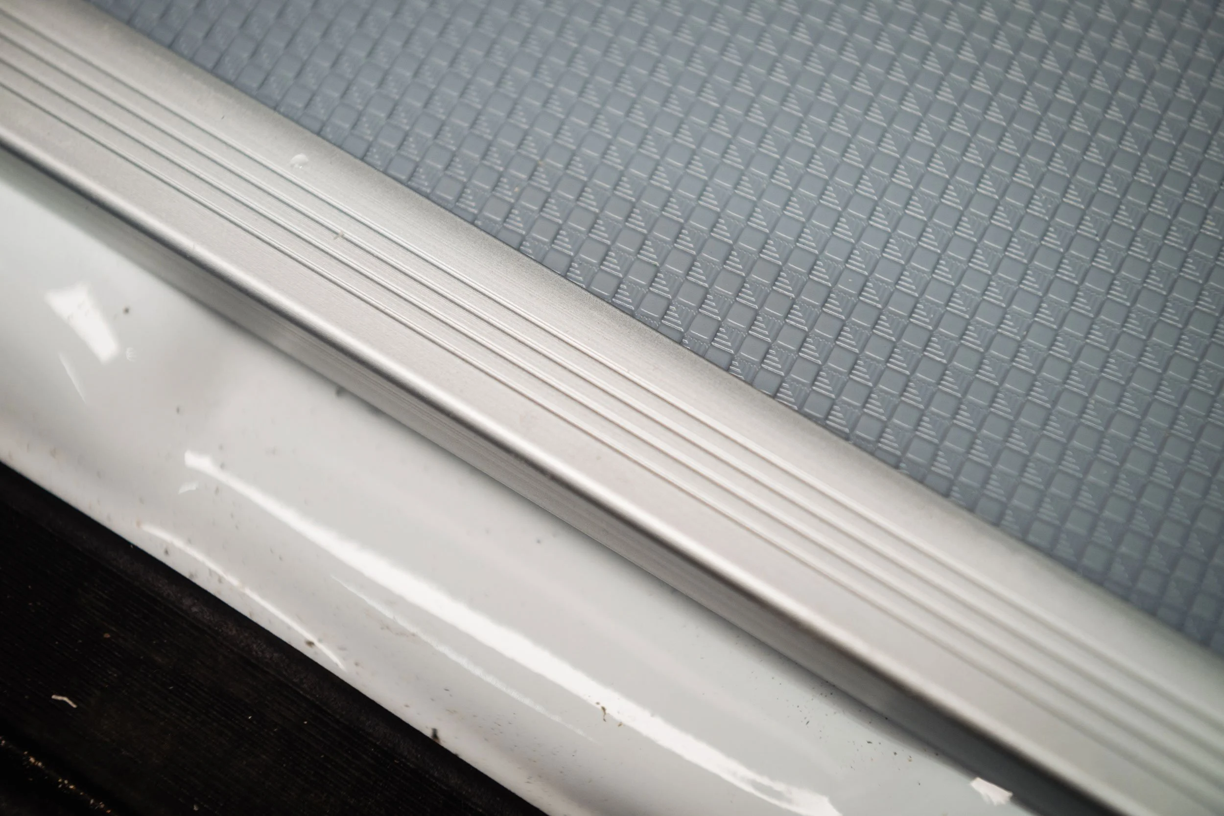 Close-up of the edge of a car's door sill with a textured gray step pad and a silver metal trim.