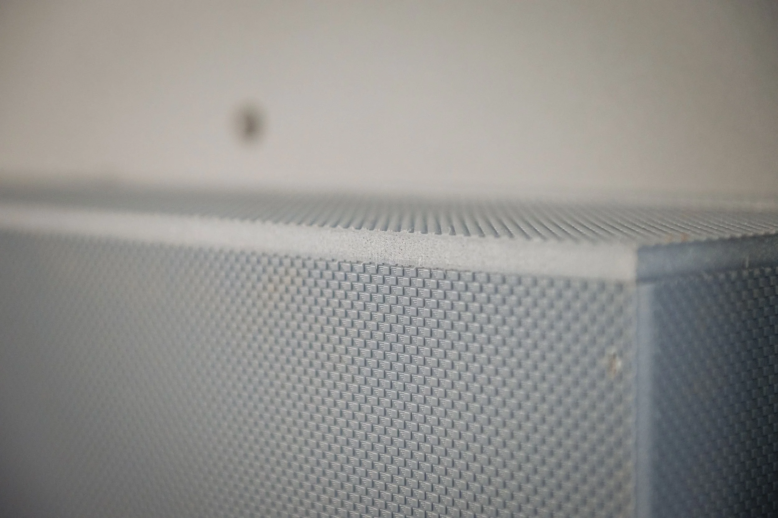 Close-up of a textured, light gray speaker grille with a corner and a small screw in the background.