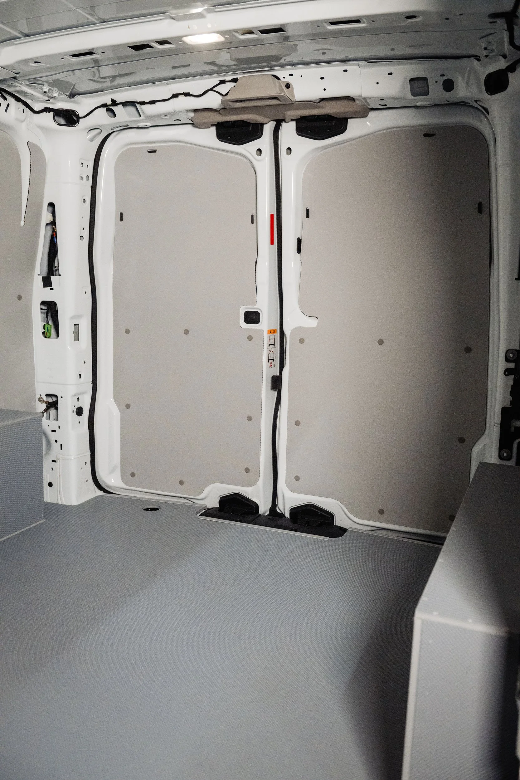 Interior view of an empty white cargo van with closed rear doors and a gray floor.