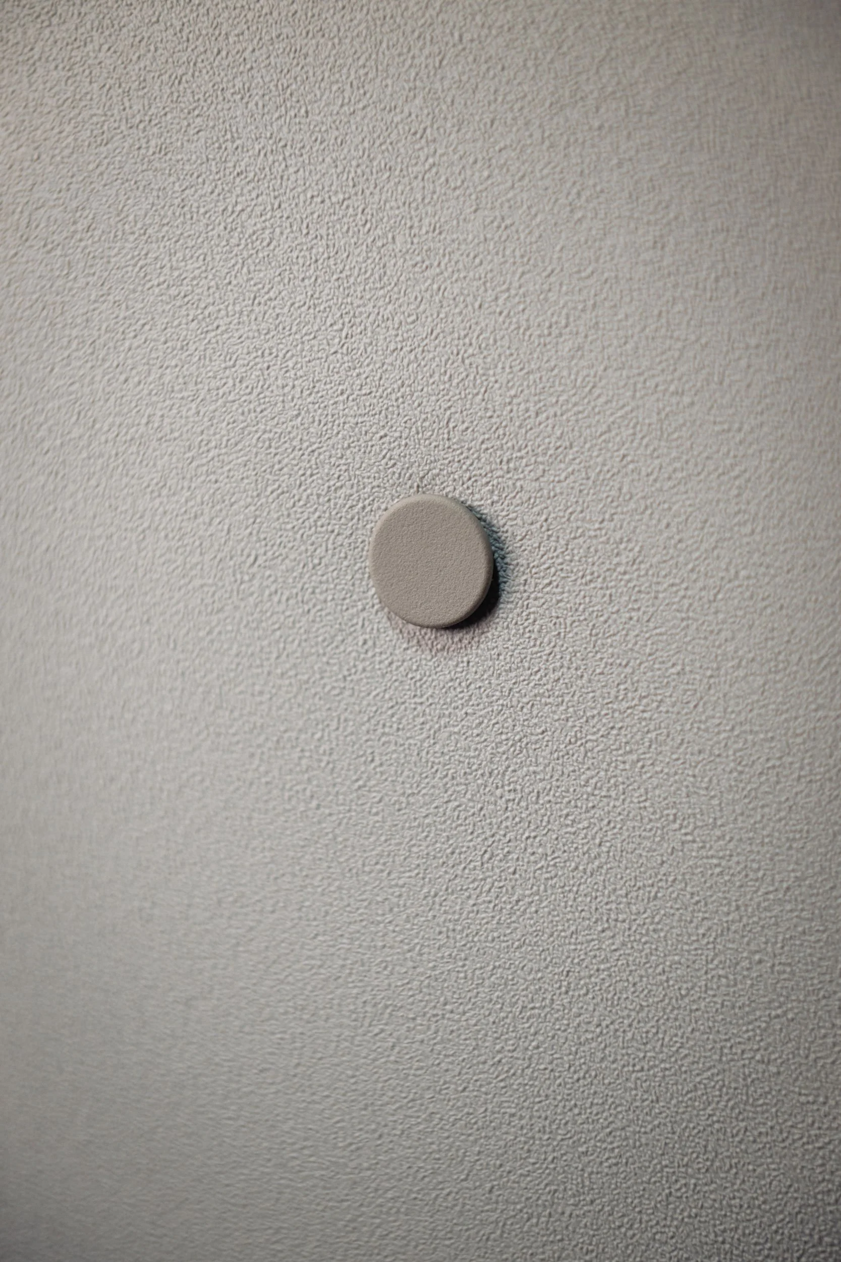 Close-up of a gray circular button on a textured light gray ceiling.