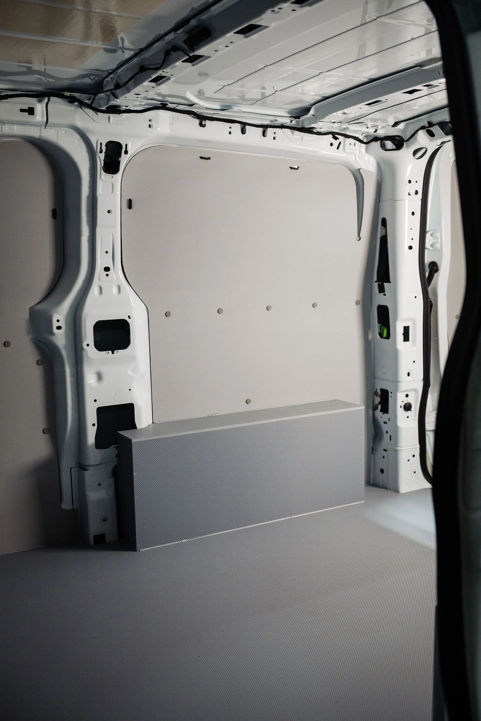 Interior of a white cargo van with blank walls and floor, no seats or cargo, with some wiring visible along the ceiling and side walls.