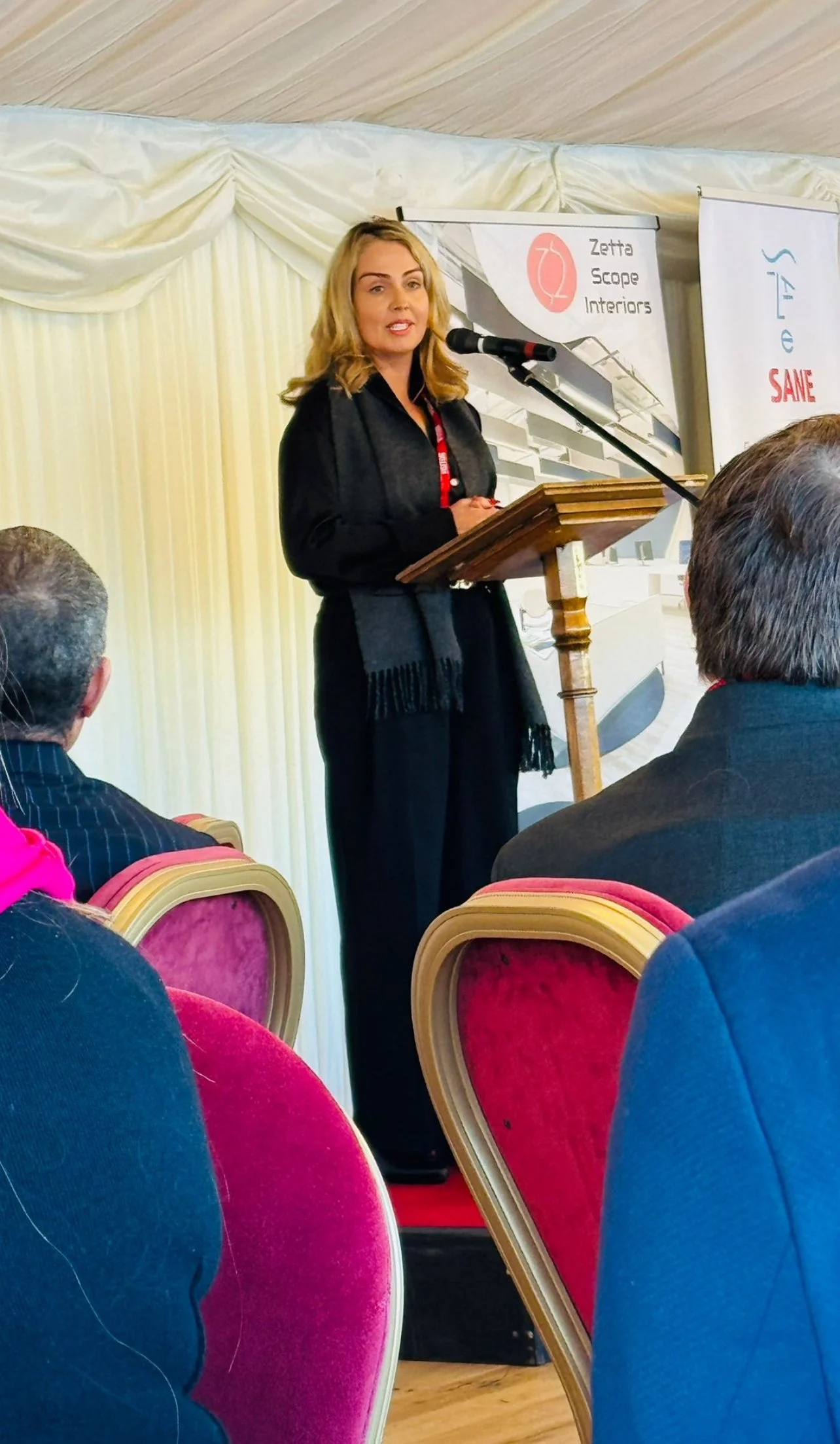 Louize Clark delivering a keynote at the Houses of Parliament — House of Lords and Commons annunciators visible
