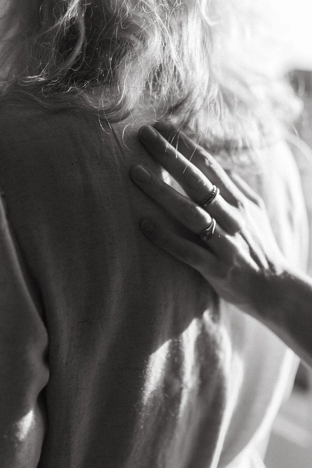 Close-up van een persoon die hun hand op de schouder legt, in zwart-wit fotografie.