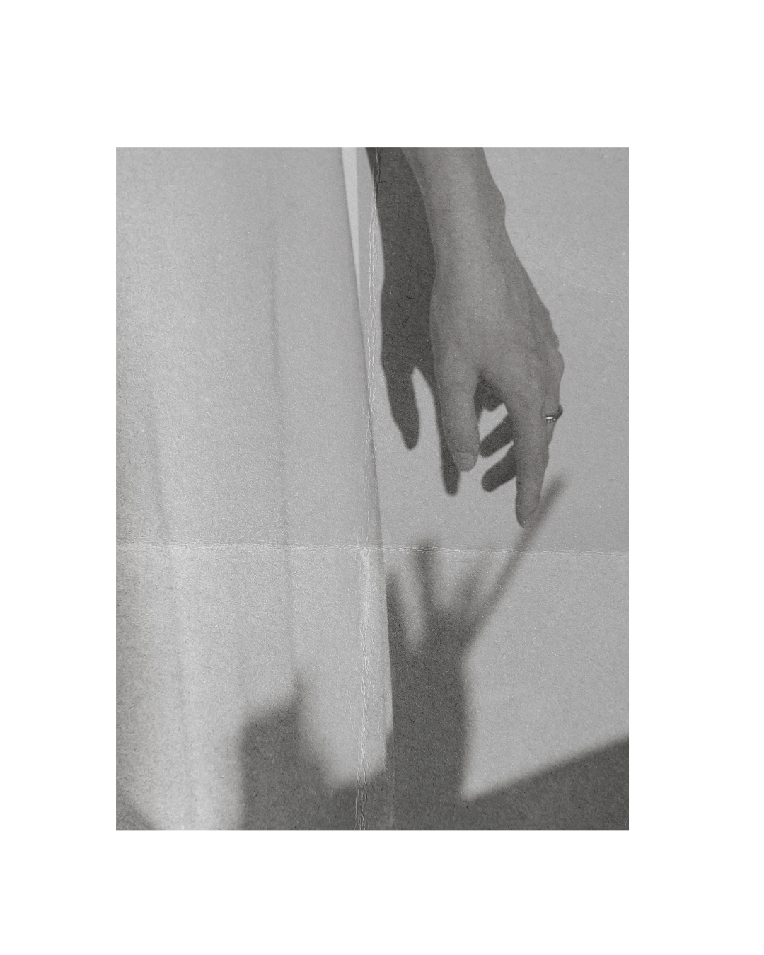 Zwart-witte foto van een hand die naar beneden wijst, de schaduw van de hand is zichtbaar op de muur erachter.