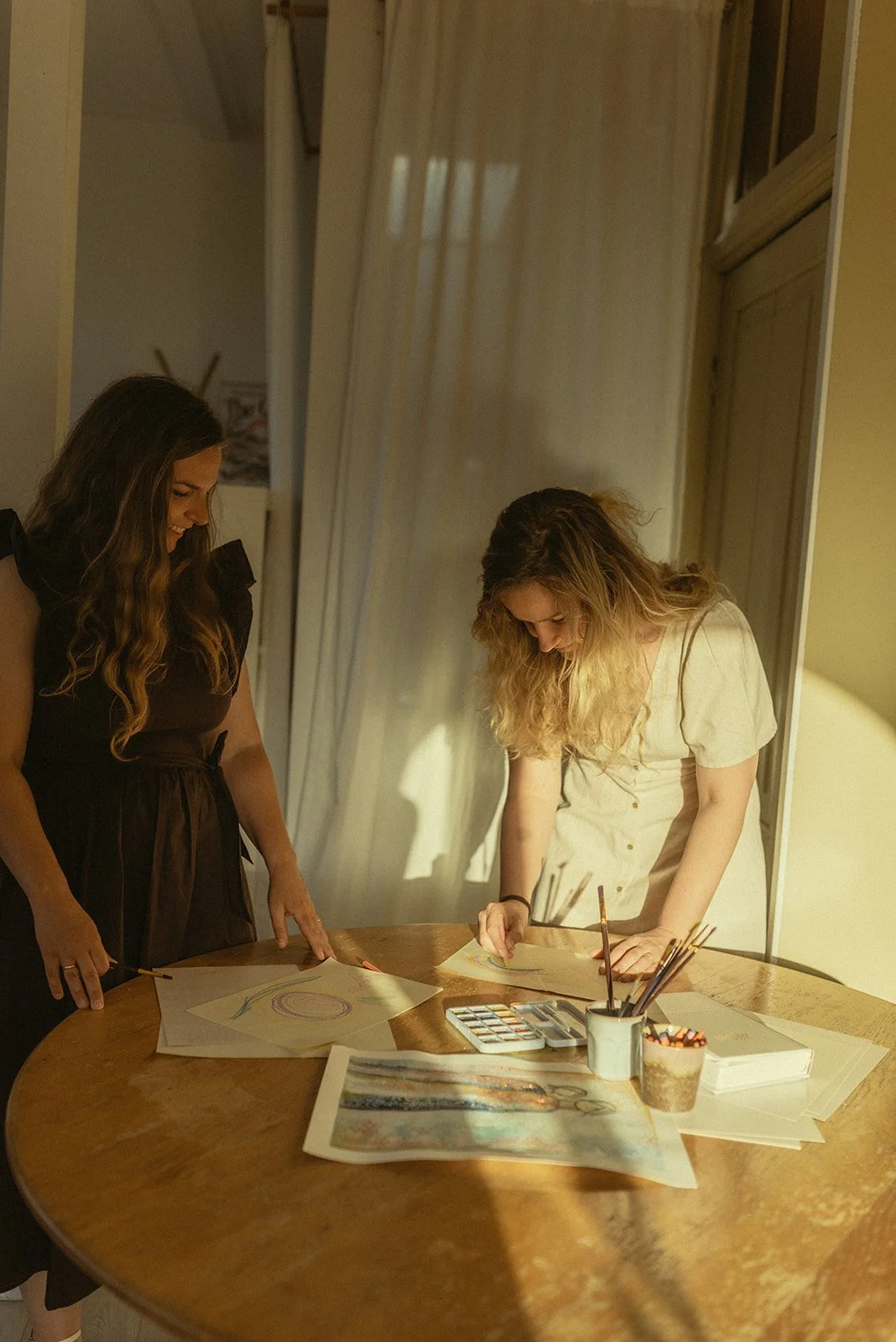 Twee vrouwen die op een tafel schilderen en tekenen met waterverf, omringd door schildermaterialen.