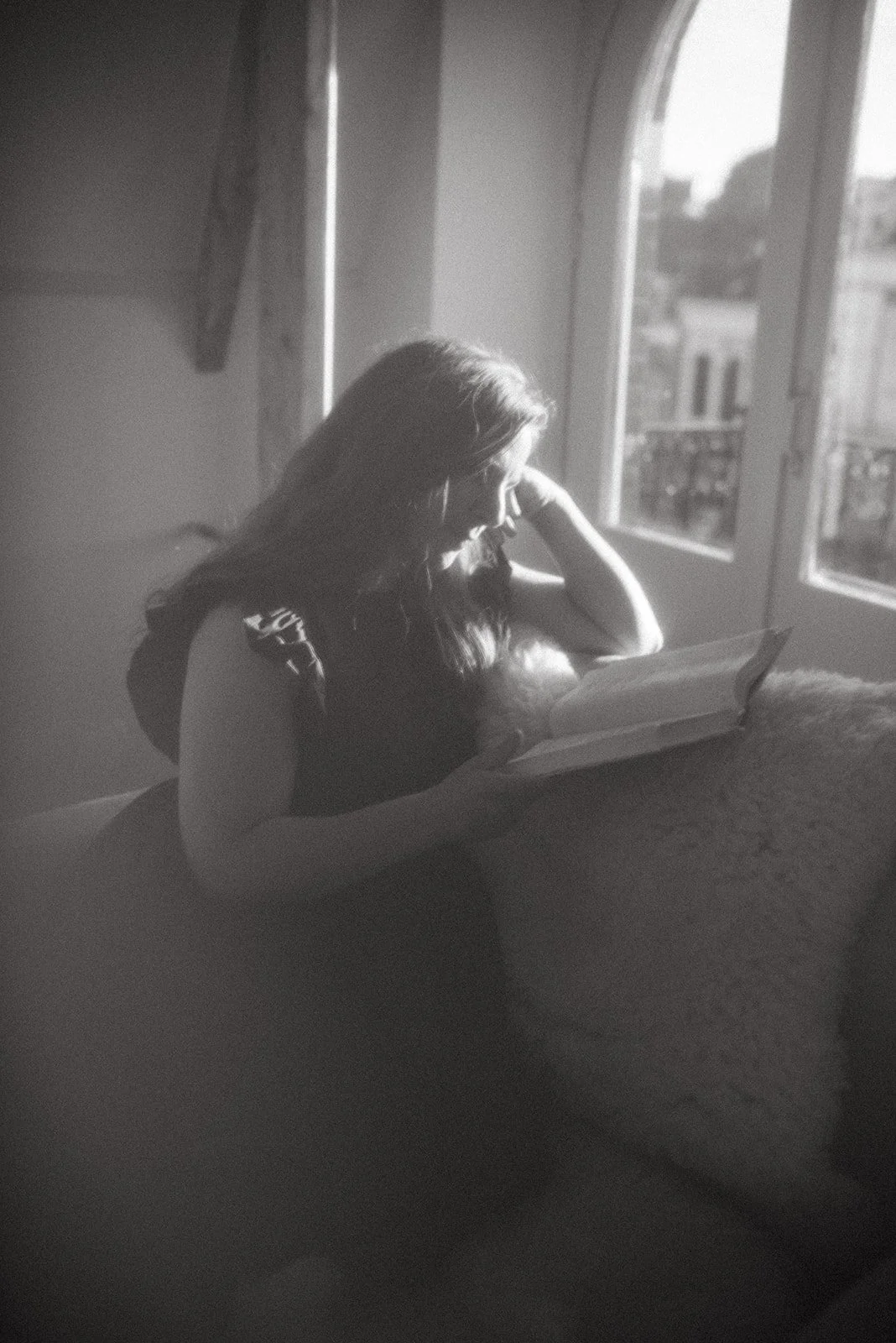 Vrouw leest boek bij raam in een zwart-wit foto.