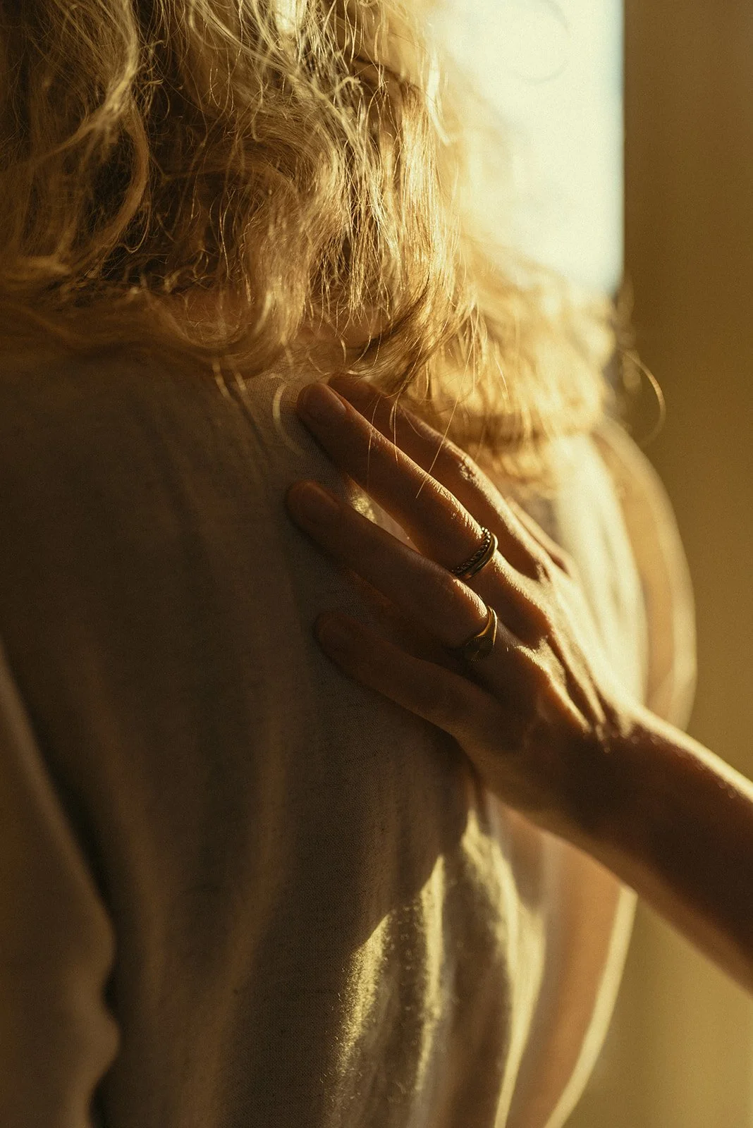Close-up van een vrouw met lang, golvend haar die haar hand op haar schouder legt, met warm licht dat haar haar en hand verlicht.