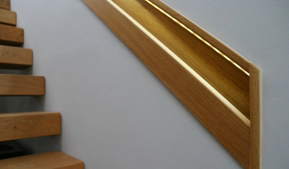 Wooden staircase handrail with built-in light strip along a plain wall.