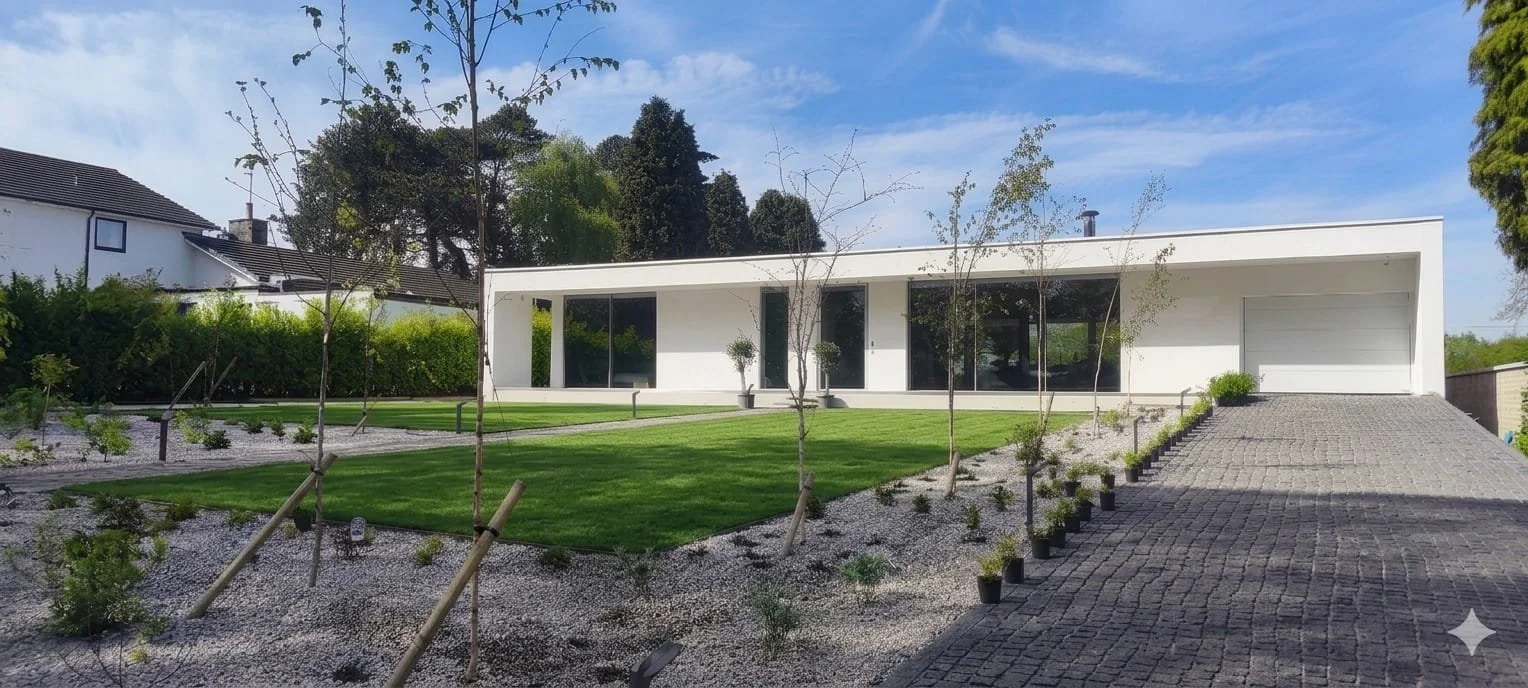Modern white house with large windows, surrounded by landscaped yard with grass, small trees, and potted plants, and a paved driveway.