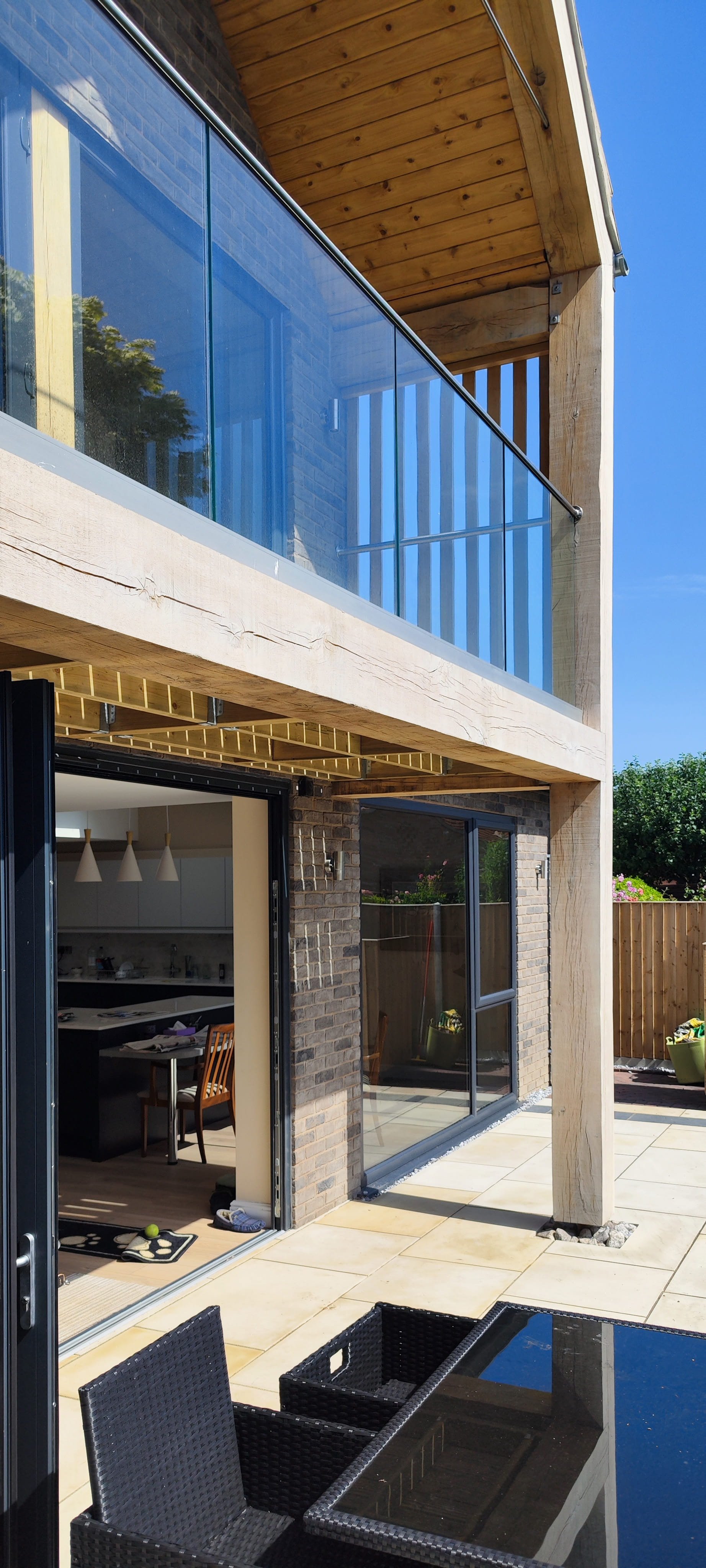 Modern two-story house with a patio, glass balcony, and sliding doors leading inside.