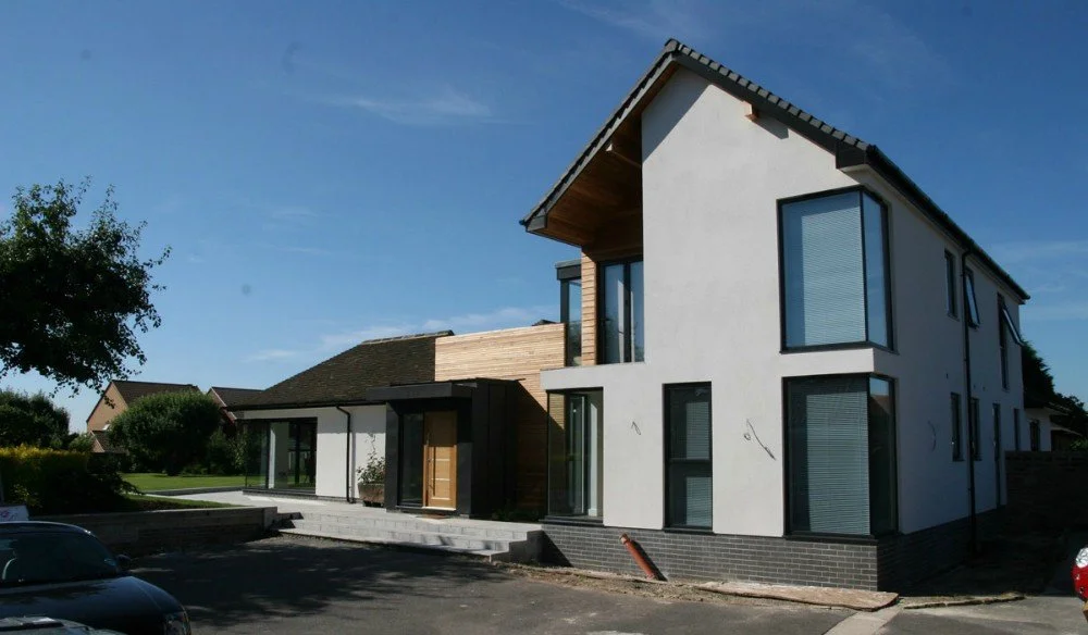 Modern two-story house with large windows, white exterior walls, and a wooden accent on the upper balcony