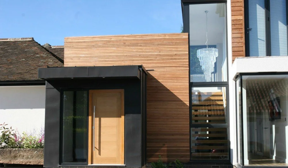 Modern house exterior with black, wood, and glass features, including a front door and large windows.