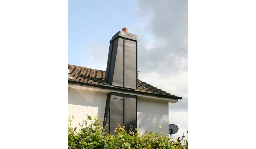 A chimney with a metal cover extending above a house roof, with a satellite dish and greenery in the foreground.