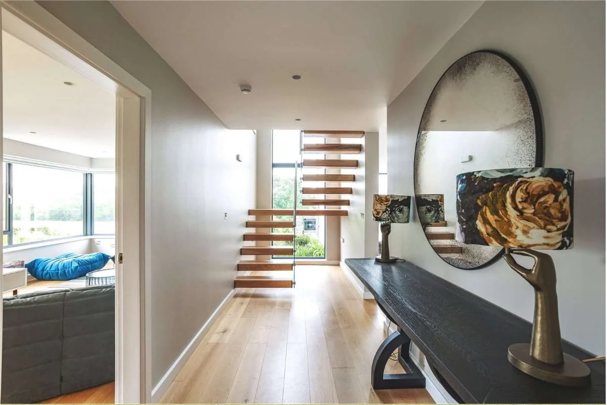 Modern entryway with wooden floating staircase, large wall mirror, and a sideboard with decorative lamps featuring artistic lamp shades.