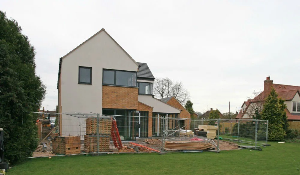 A house under construction with brick and white exterior, construction materials, and fencing surrounding the site.