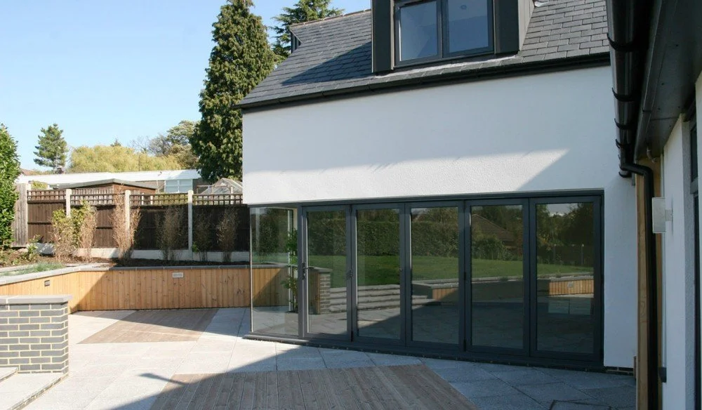Modern house with large glass sliding doors leading to a backyard with wooden deck and fenced garden