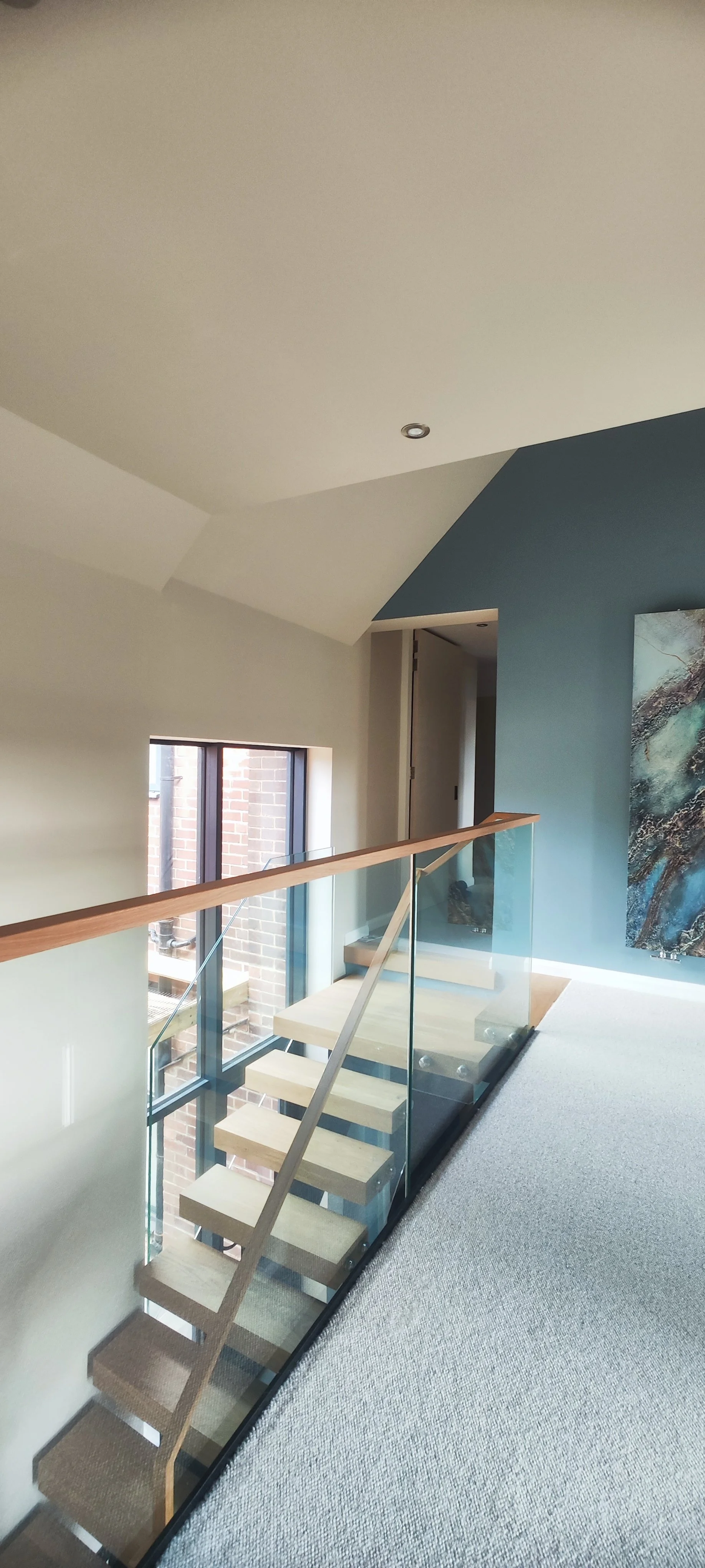Interior view of a modern upstairs hallway with a staircase, railing, and partial wall with artwork.