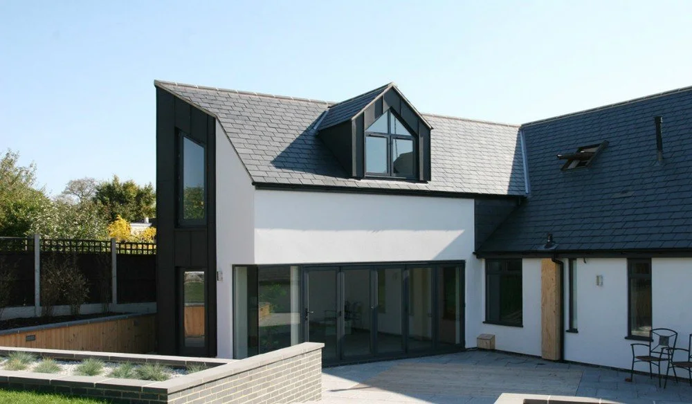Modern two-story house with black and white exterior, multiple large windows, a pitched roof, and a small balcony.